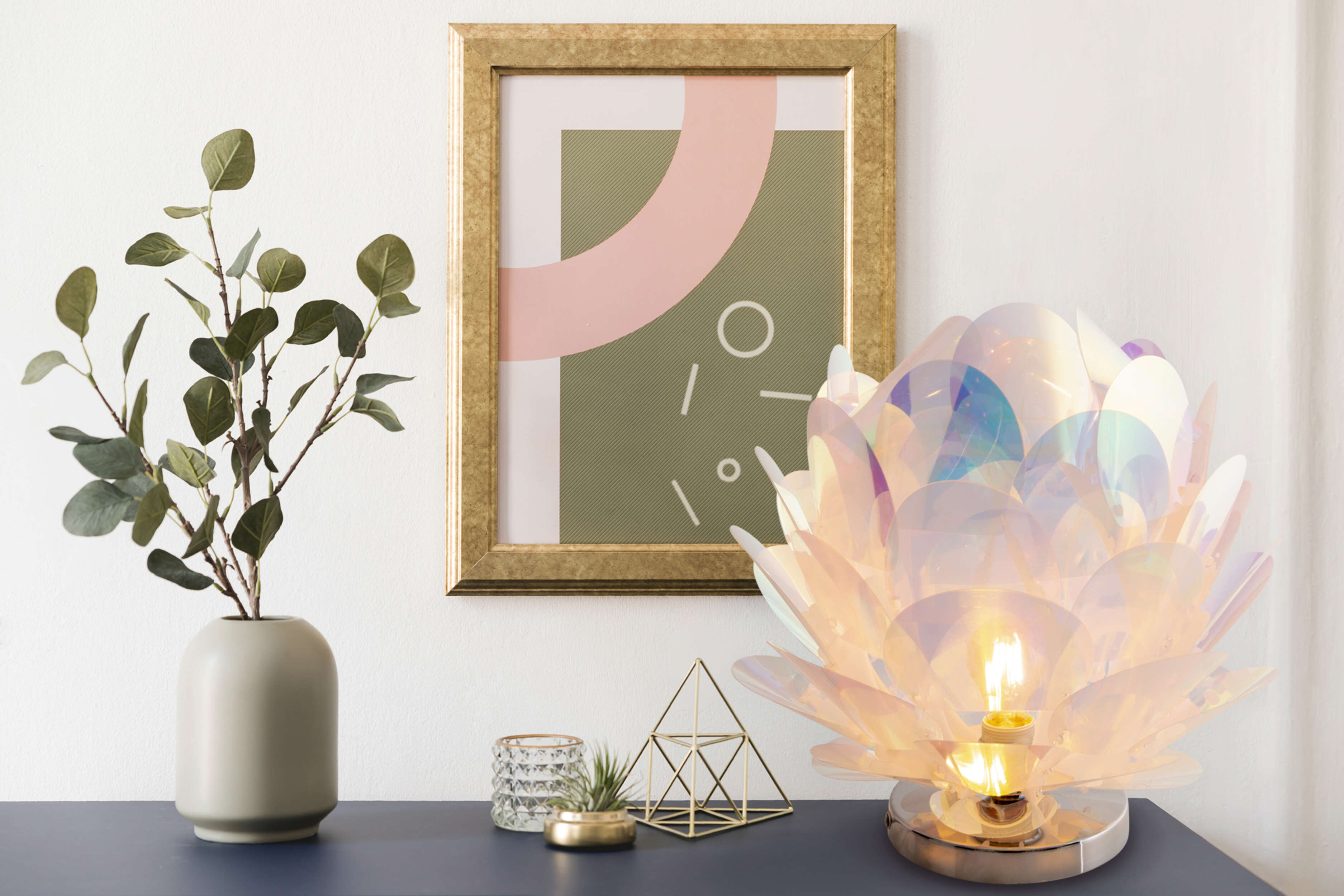 Ein Stillleben mit Lampe, gerahmtem Bild, Vase mit Blättern und goldener geometrischer Form.