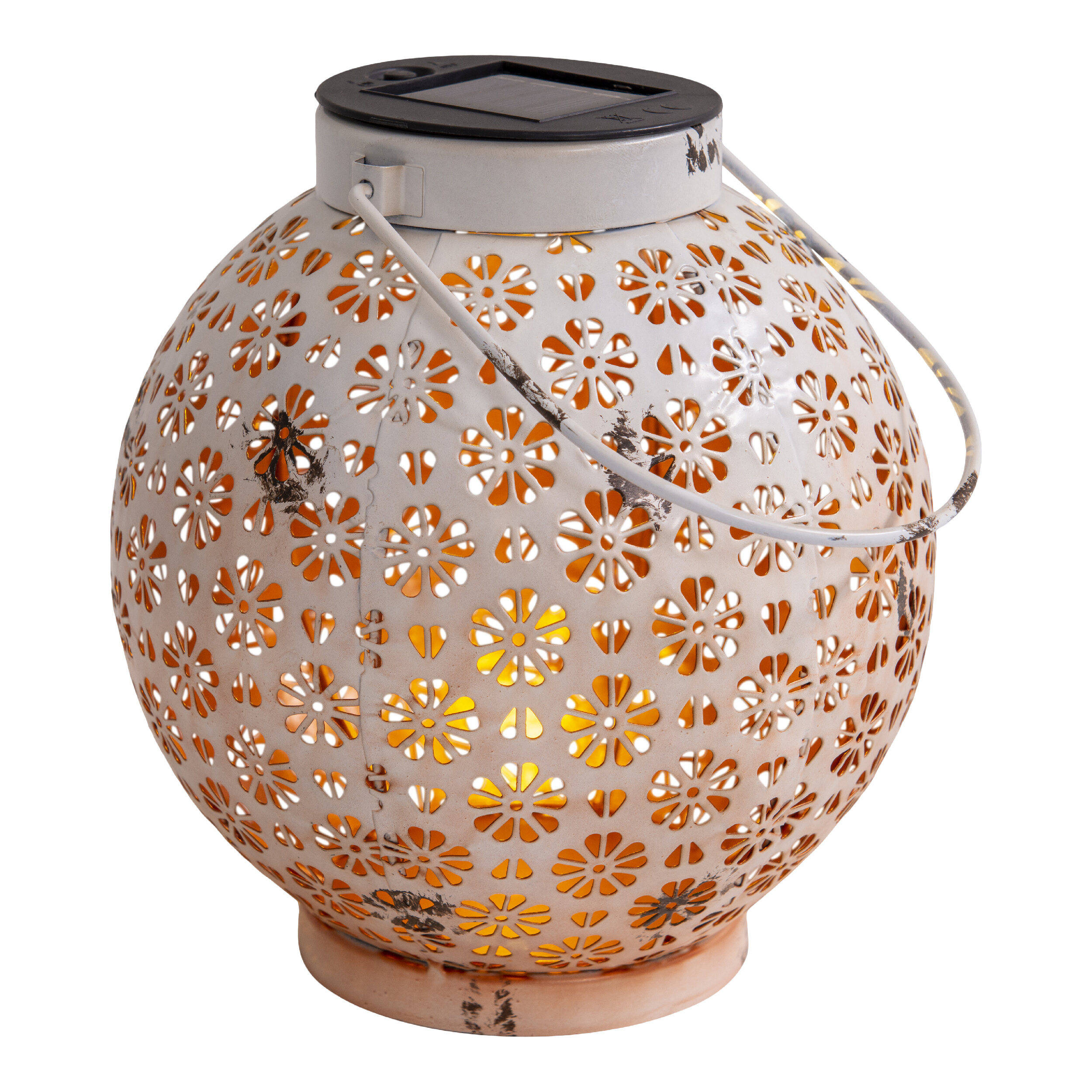 Weiße Solar-Laterne mit Blumenausschnitten, Griff und dunklem Deckel, beleuchtet mit orangefarbenem Schein.