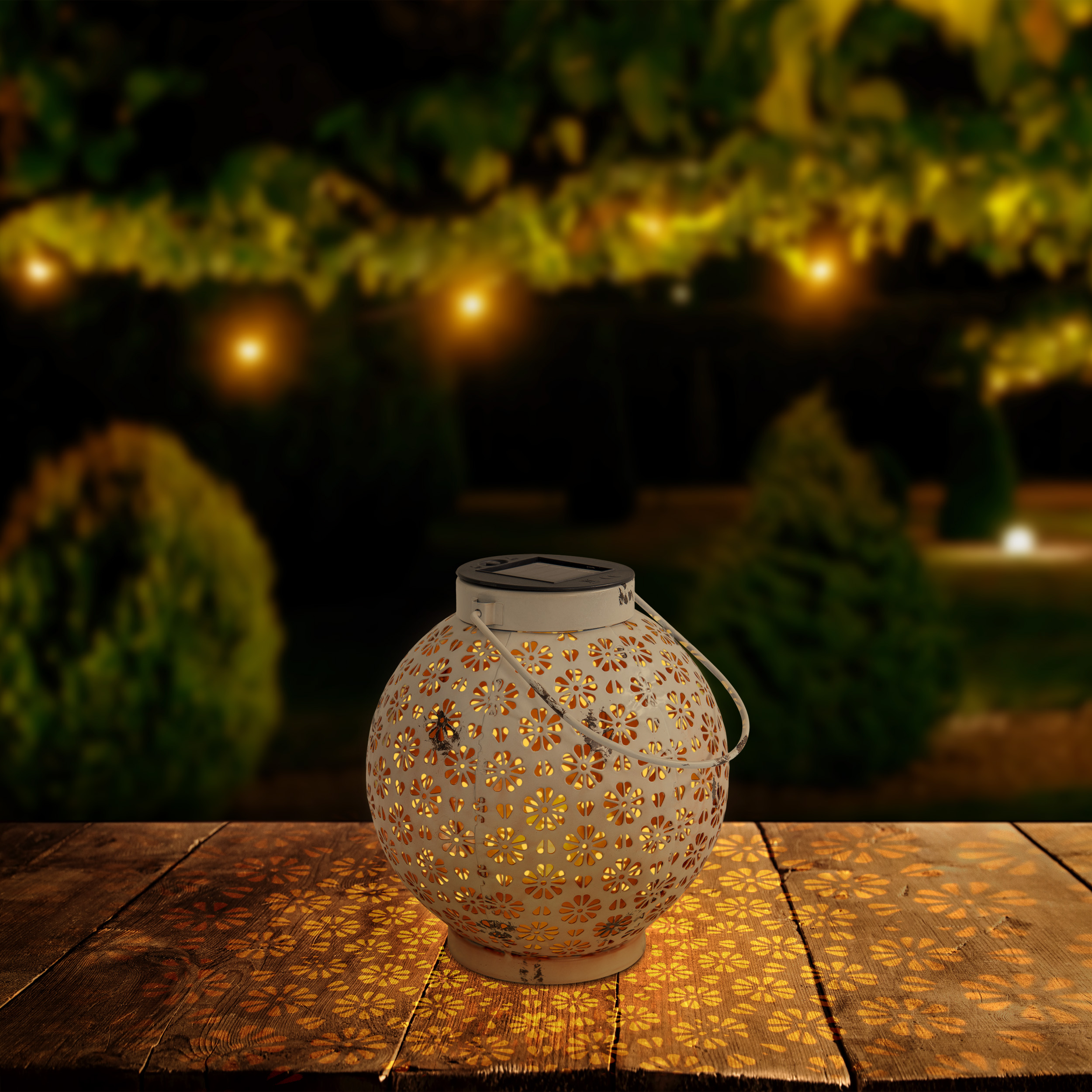 Eine weiße Solar-Laterne auf einem Holztisch bei Nacht, mit verschwommenem Gartenhintergrund und Lichtern.
