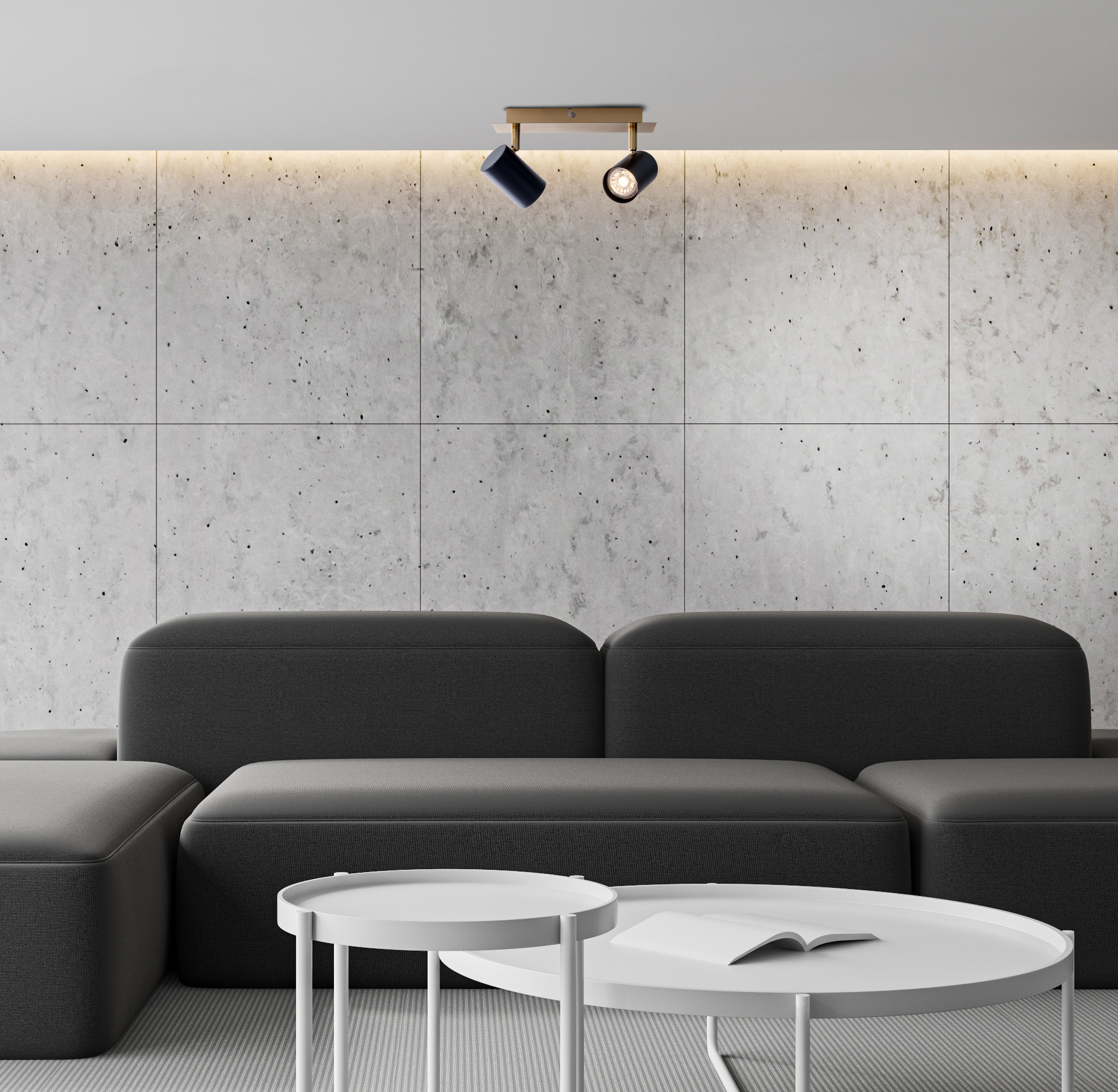 Modernes Wohnzimmer mit grauem Sofa, Betonwand, weißen Tischen und zwei schwarzen Strahlern.