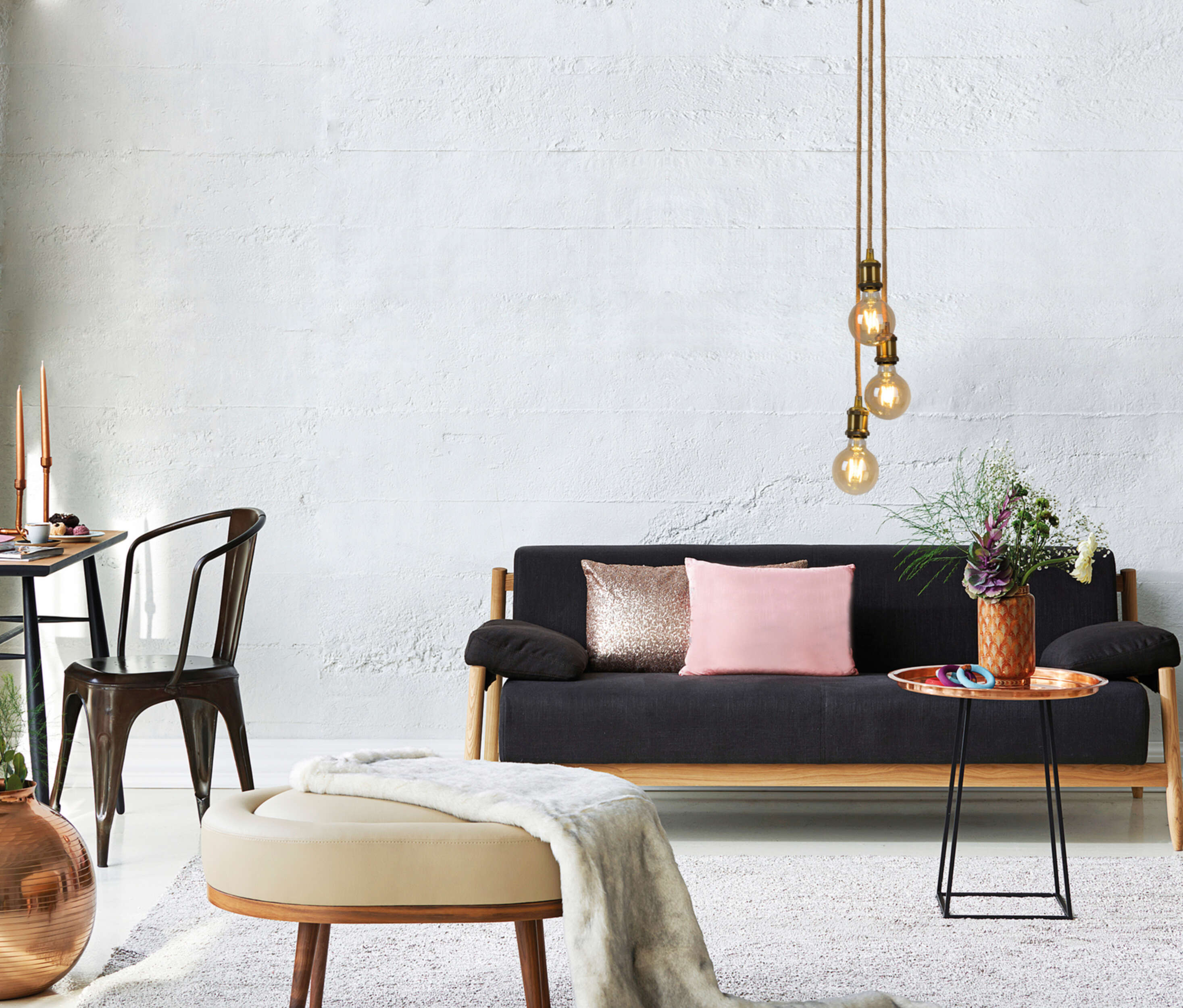 Wohnzimmer mit schwarzem Sofa, Kissen, Couchtisch und weißer Wand. Dekorative Gegenstände ausgestellt.