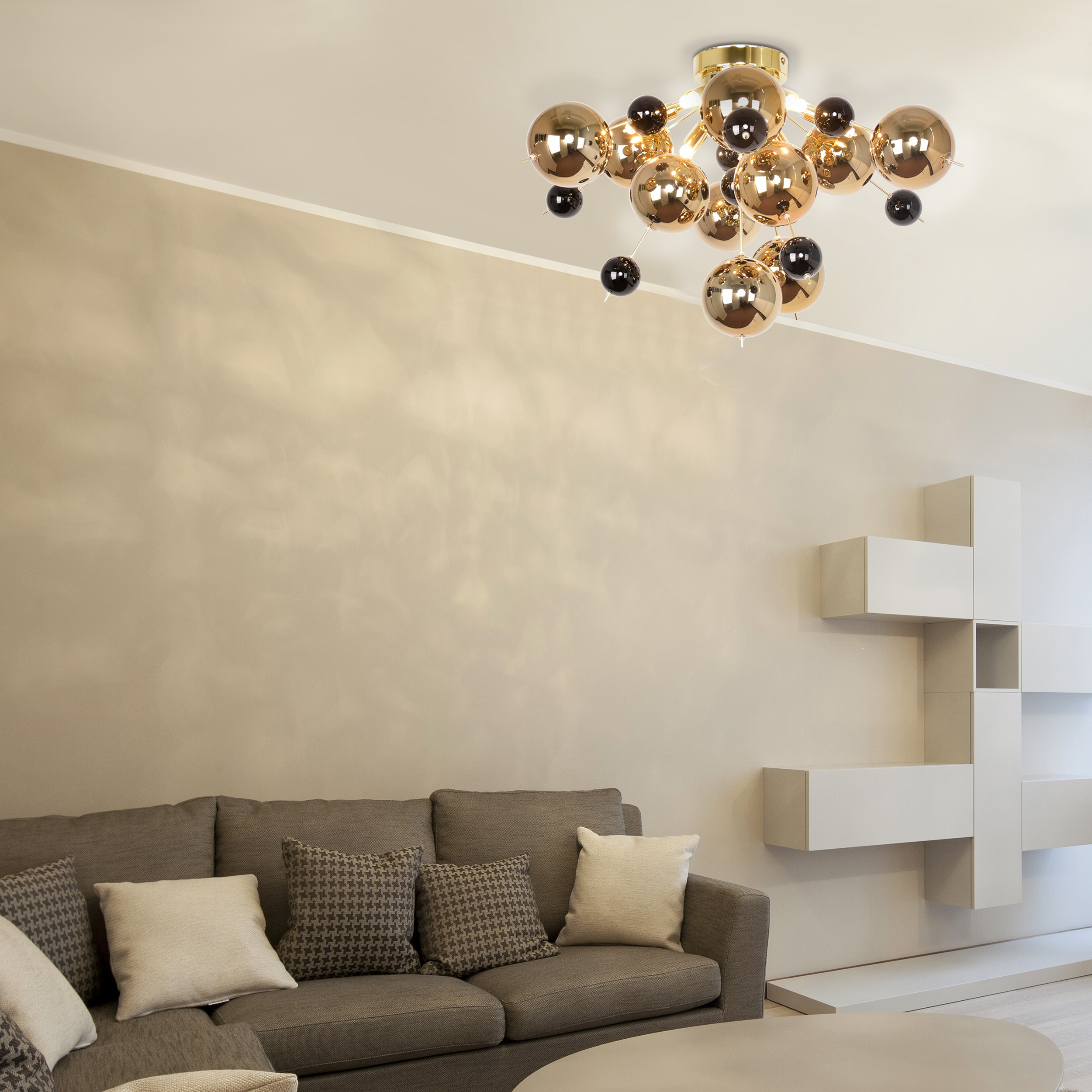 Salon avec lustre moderne à sphères dorées, canapé et étagères murales.