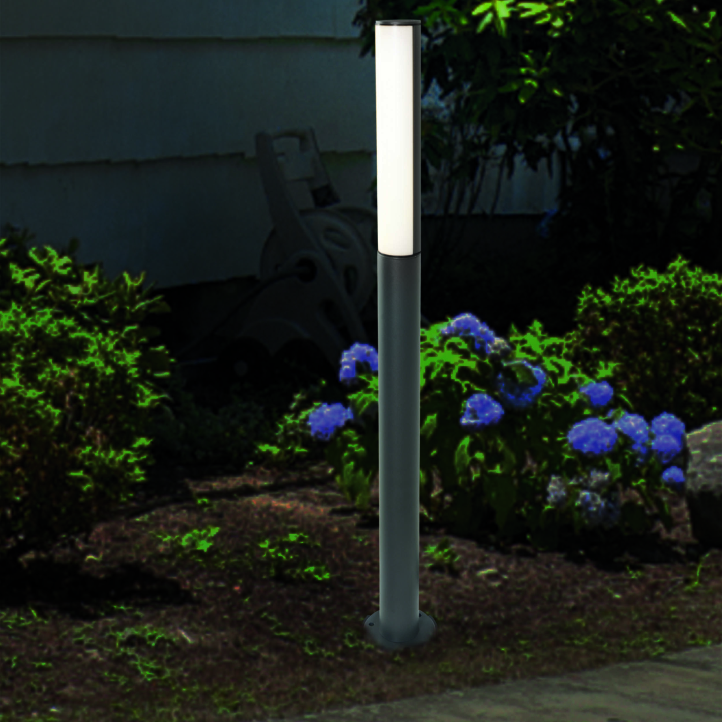Hohe Außenlampe mit weißem Licht, umgeben von grünen Büschen und blauen Blumen.