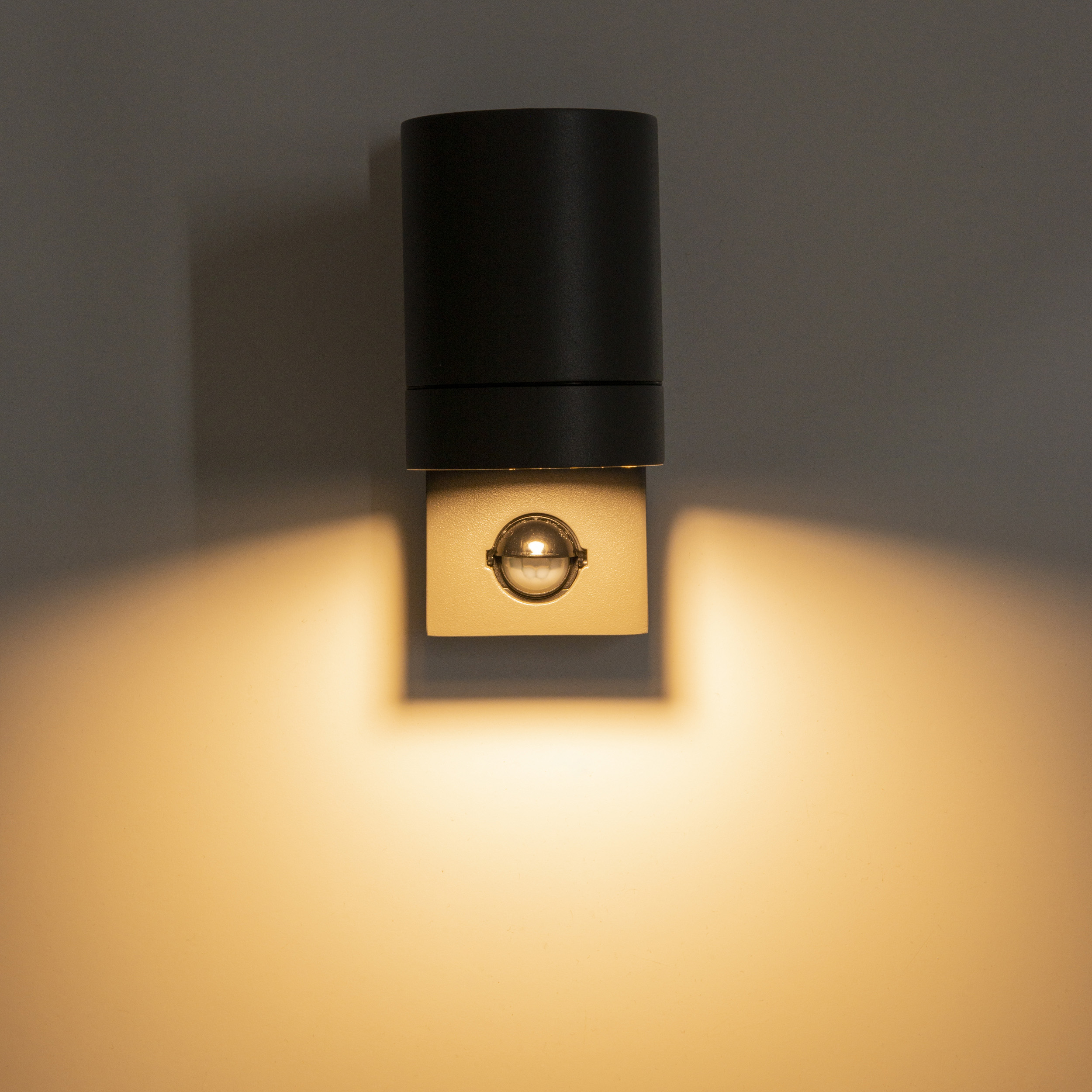 Moderne Wandleuchte in Schwarz und Gold, die die Wand darunter beleuchtet.