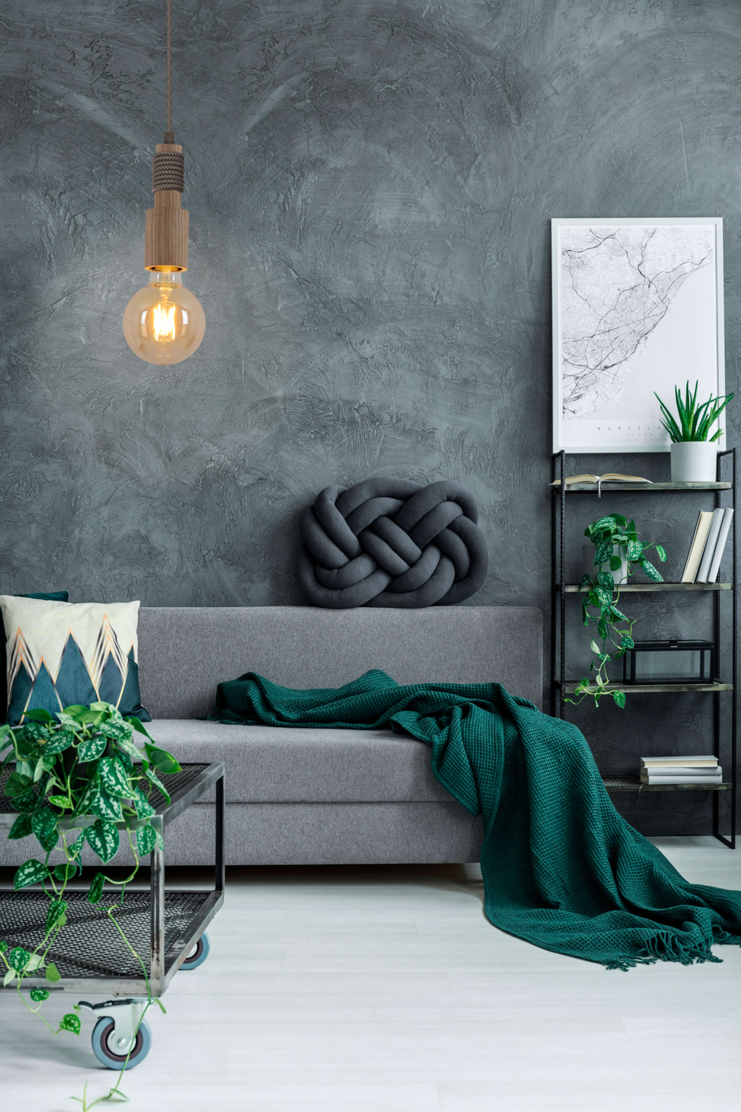 Gemütliches Wohnzimmer mit grauem Sofa, grüner Decke, Pflanzen und hängender Glühbirne.