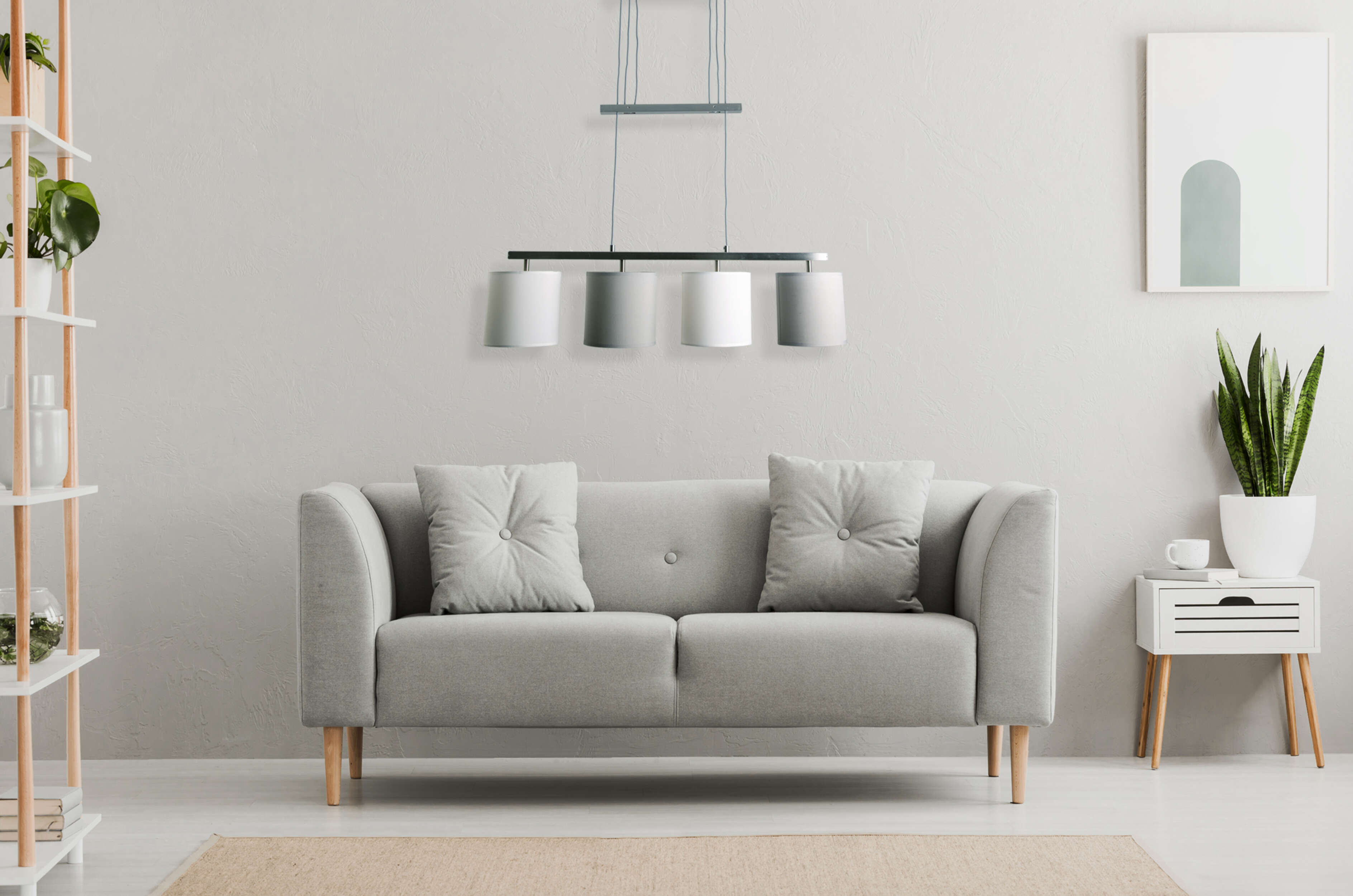 Innenszene mit grauem Sofa, Kissen, Teppich, Bücherregal und einer Hängeleuchte.