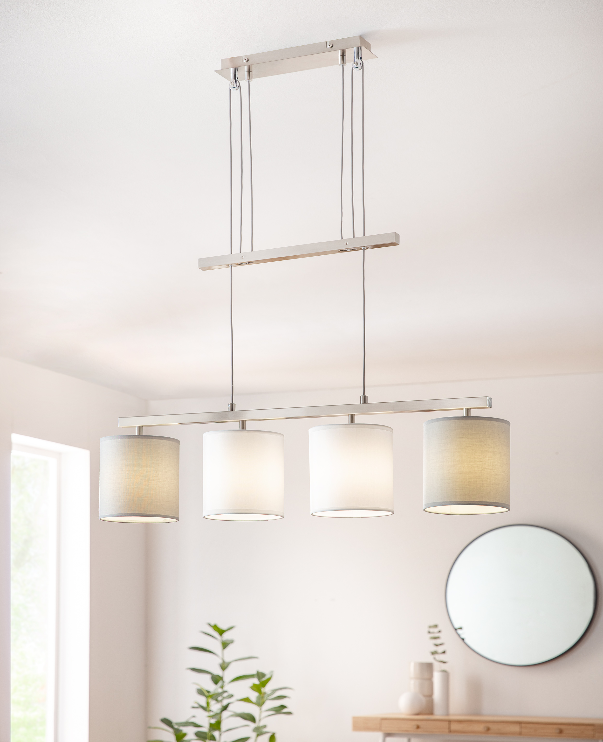 Eine moderne Pendelleuchte mit vier zylindrischen Schirmen. Das Licht hängt von der Decke.