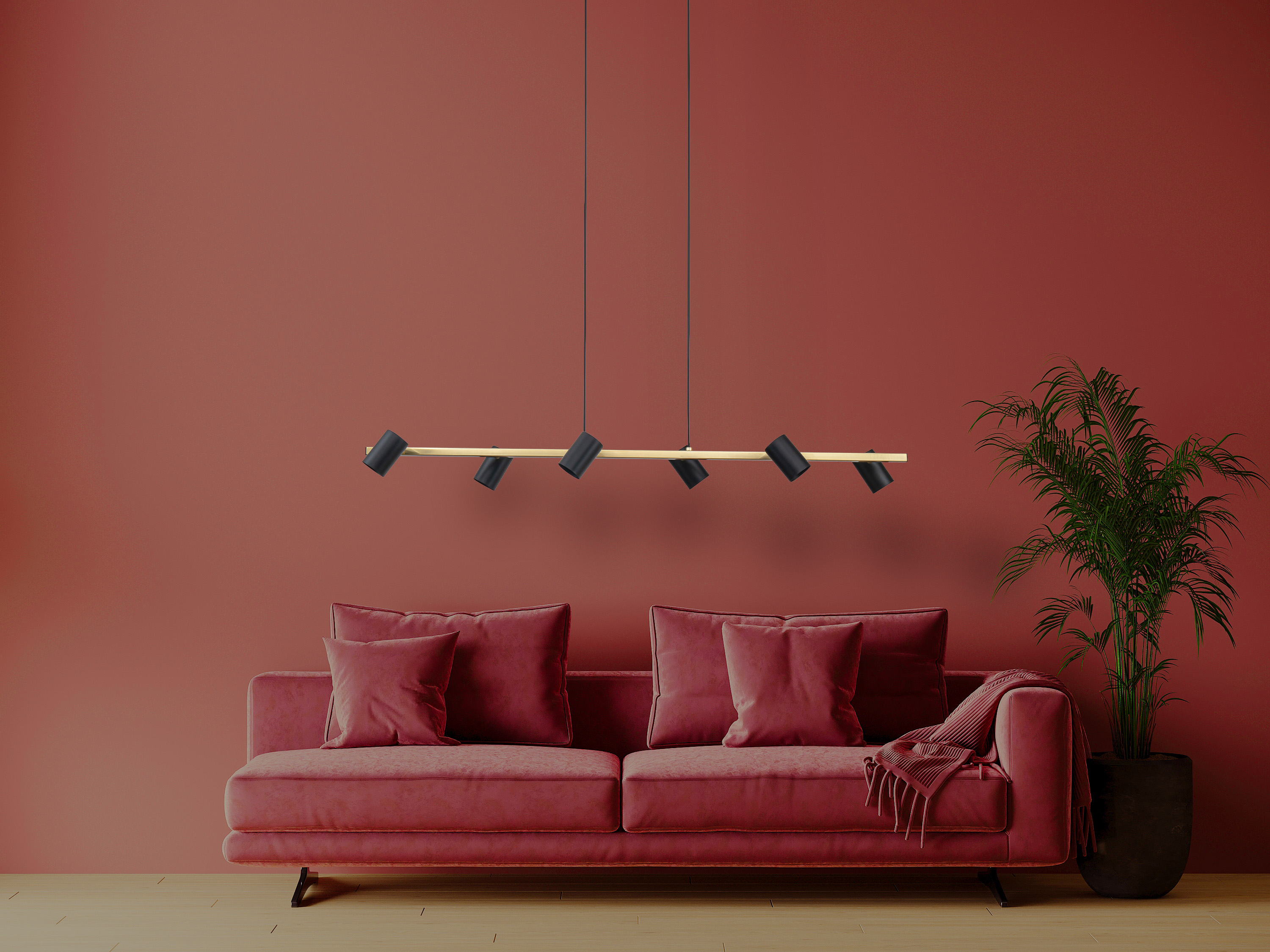 Ein rotes Sofa mit roten Kissen, eine Pflanze und eine Hängeleuchte vor einer roten Wand.
