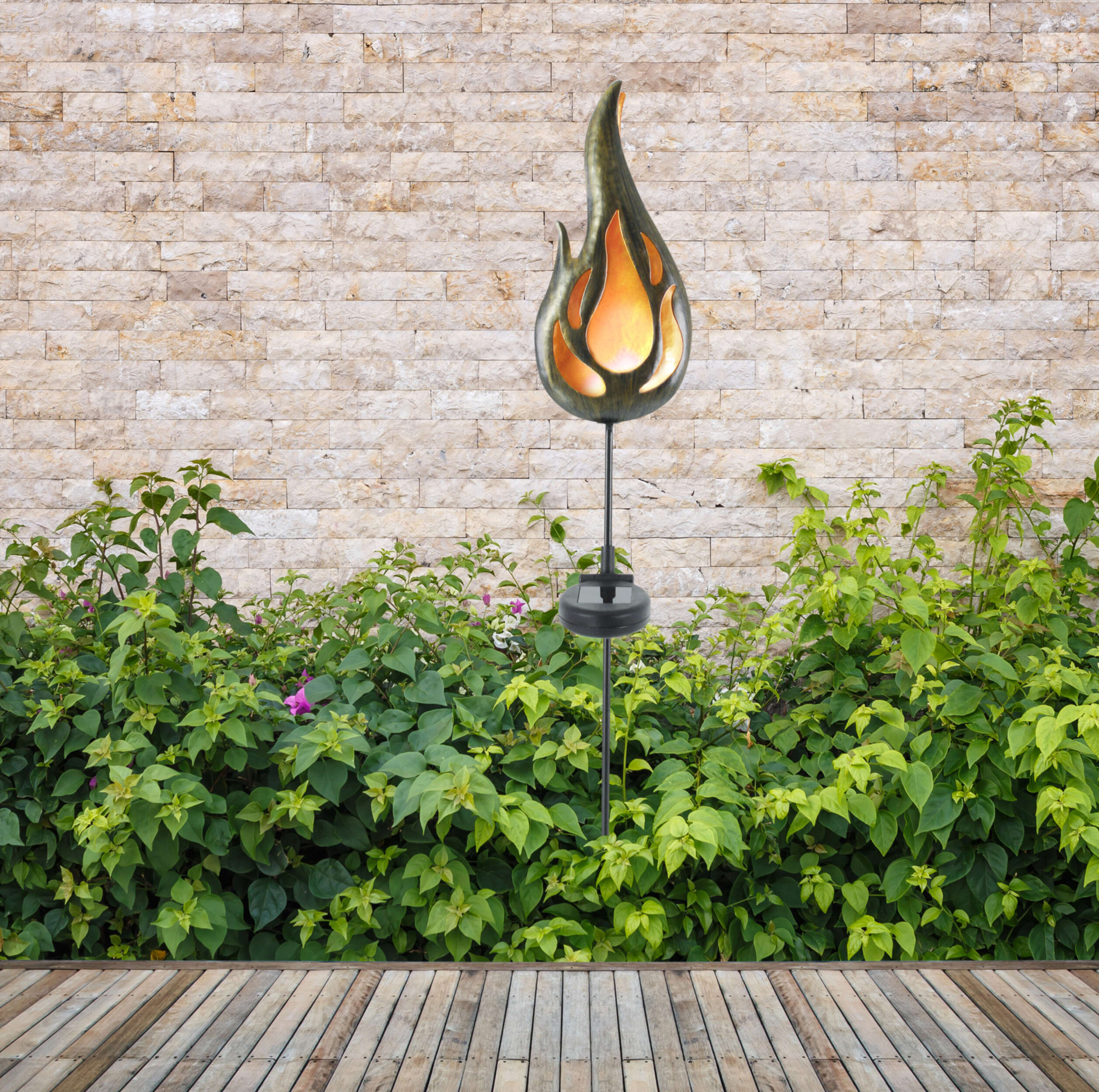 Metall-Flammenskulptur im Freien auf einem Holzdeck, mit grünen Pflanzen.