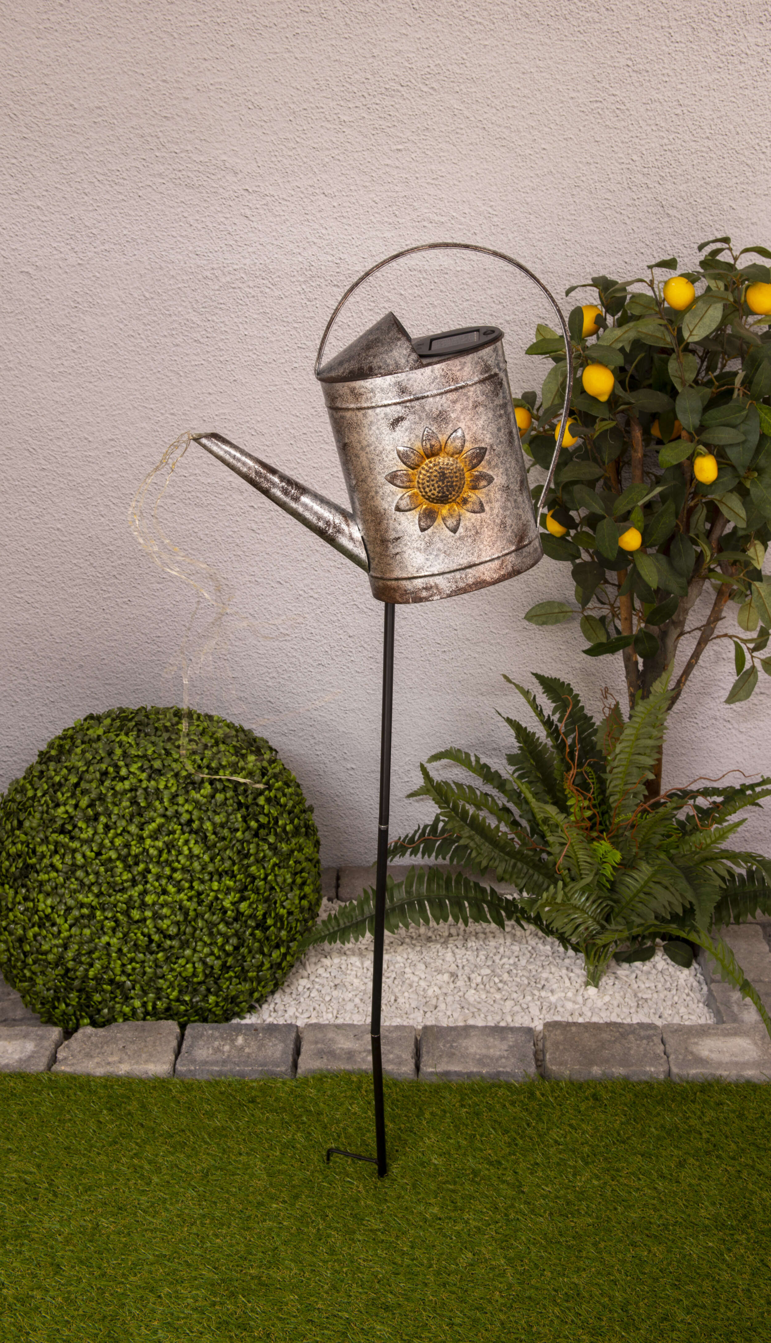 Ein solarbetriebener Gießkannen-Gartenpfahl mit Sonnenblume und Lichterketten.