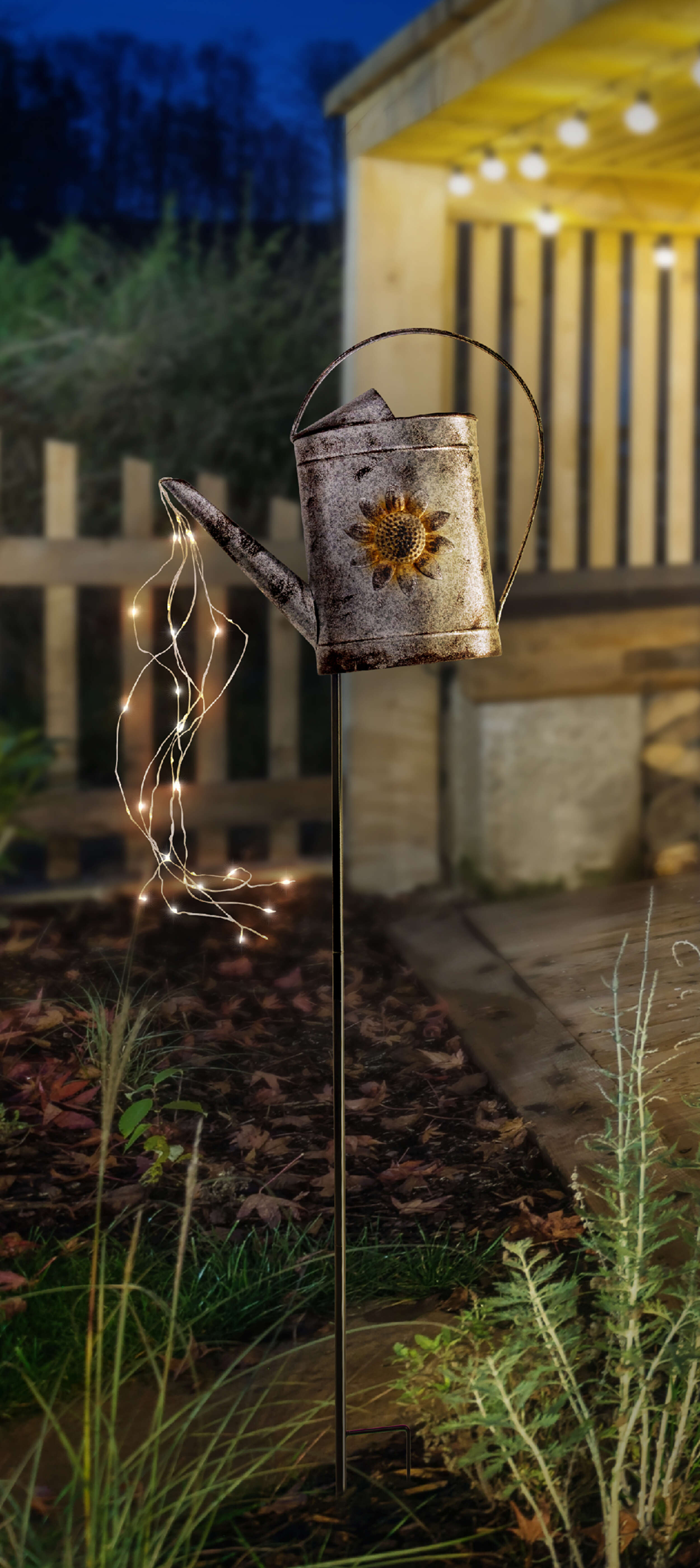 Metall-Gießkanne mit Lichtern in einem Garten bei Nacht. Sonnenblumen-Dekoration.