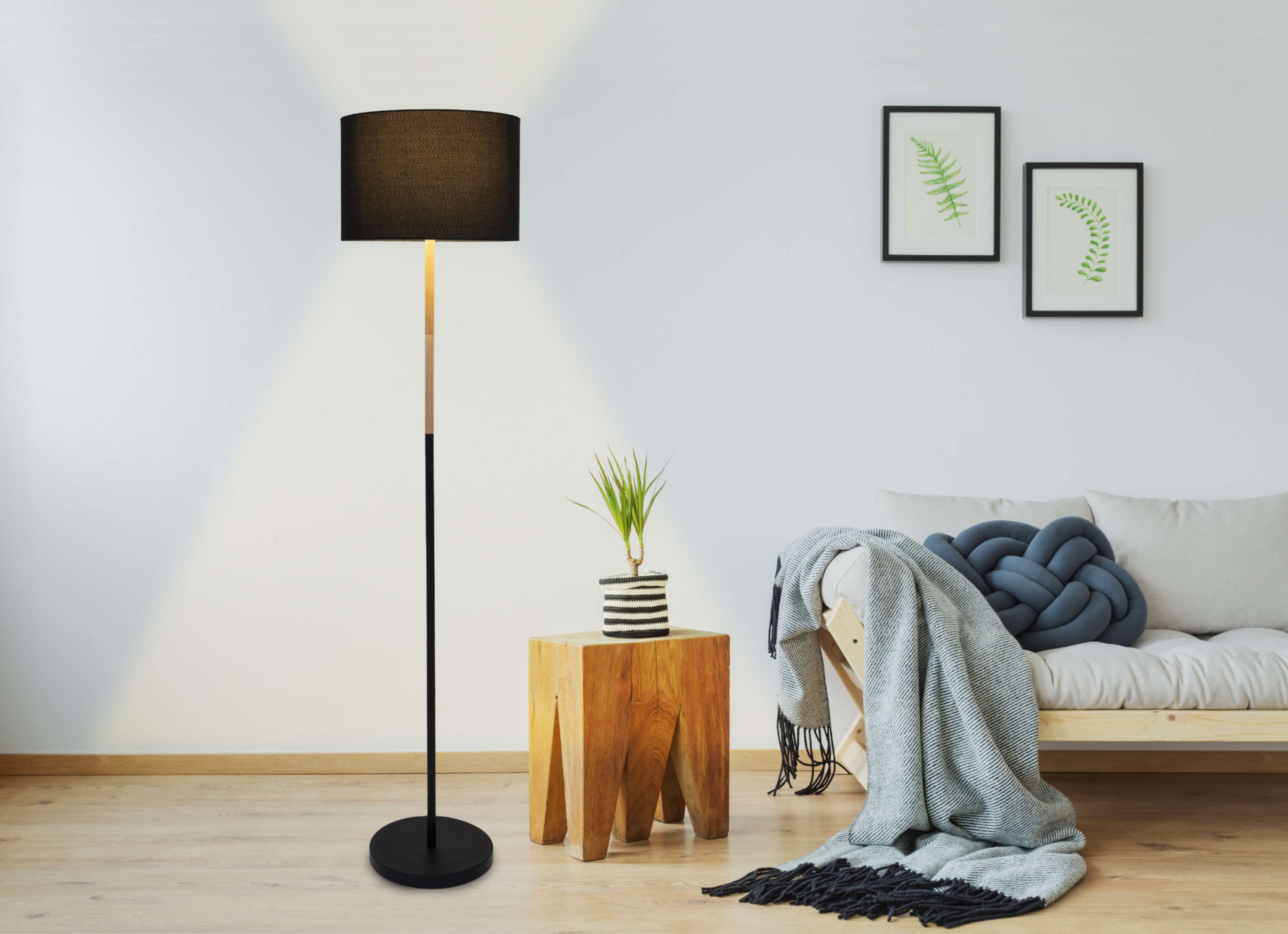 Lampadaire à côté d'un tabouret en bois et d'un canapé. Lampe noire, une couverture à carreaux et deux photos.