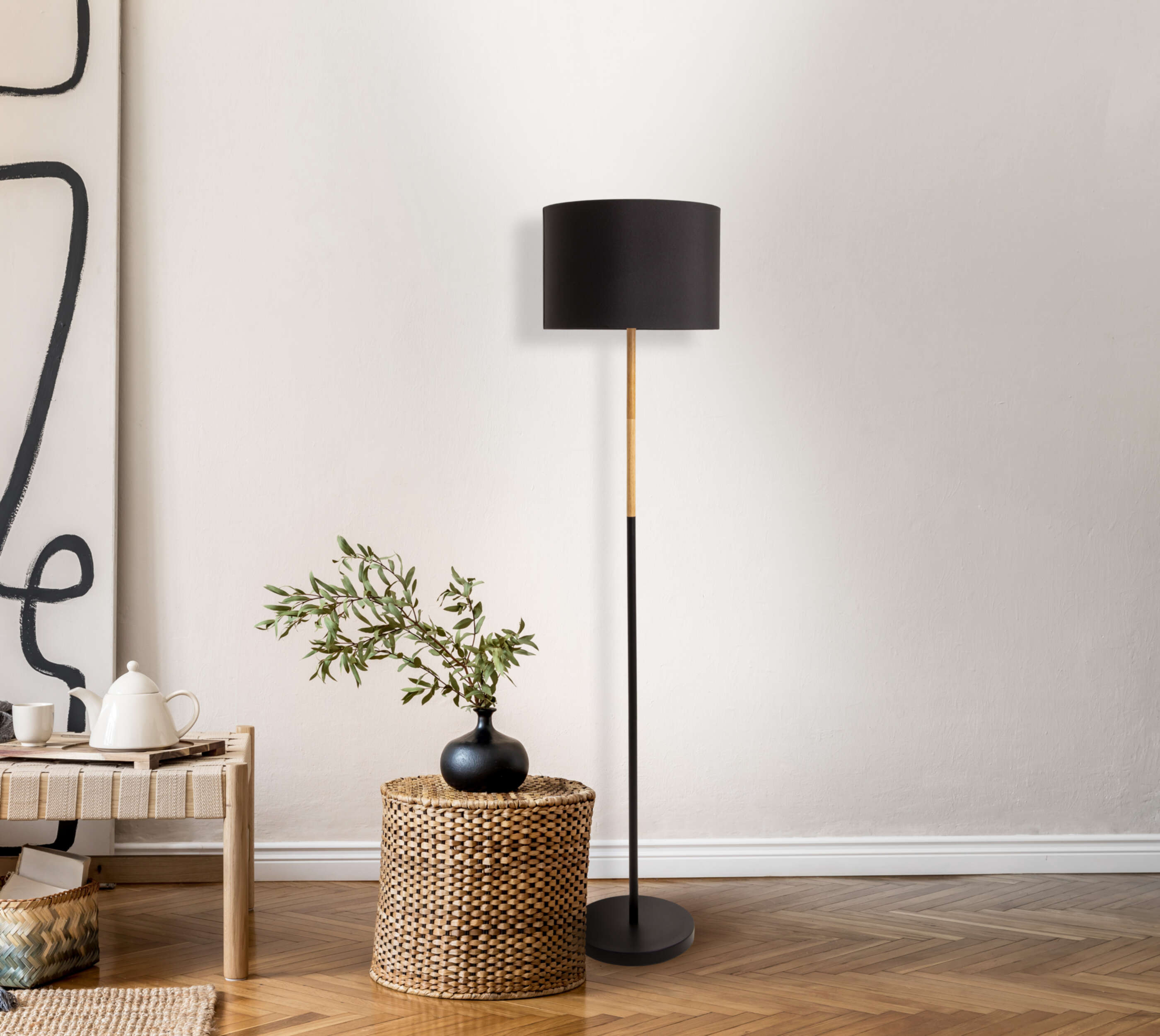 Lampadaire noir avec abat-jour, vase avec feuilles et panier en osier.