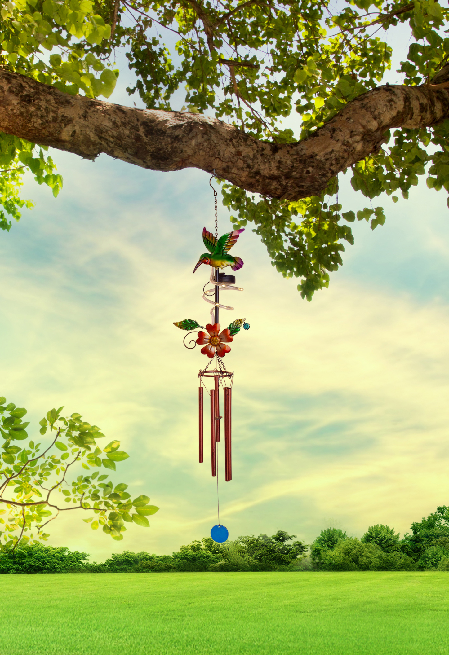 Kolibri-Windspiel, das an einem Baum hängt, grünes Gras, blauer Himmel.