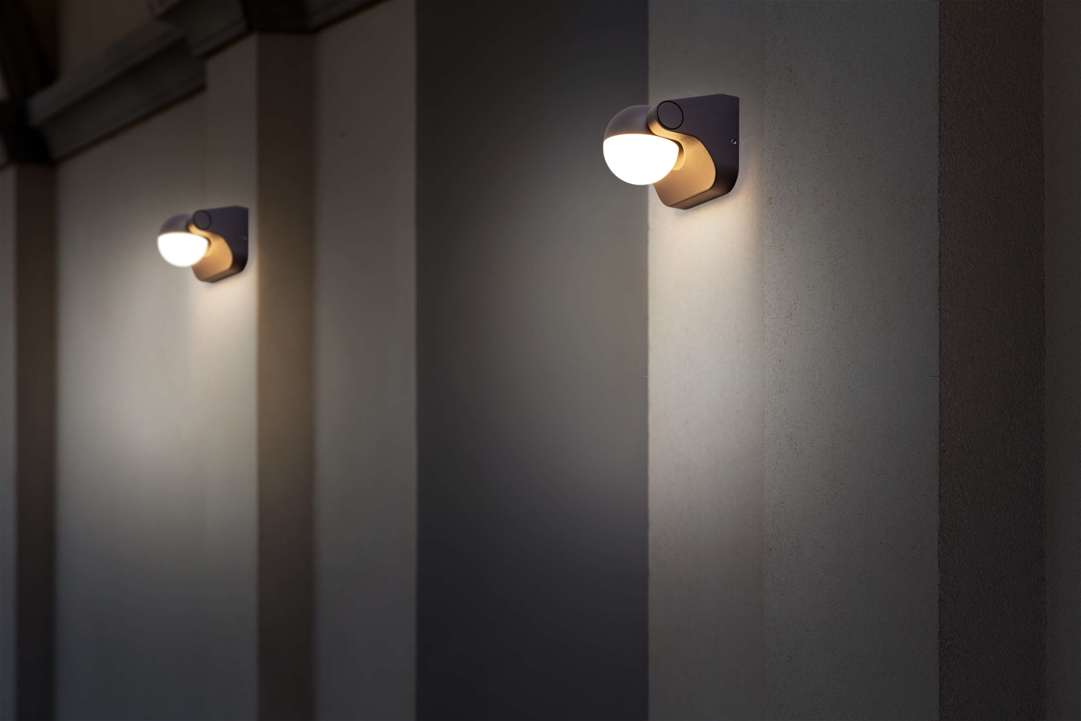 Zwei Wandleuchten an einer Wand. Die Leuchten sind halbkreisförmig und strahlen nach unten.