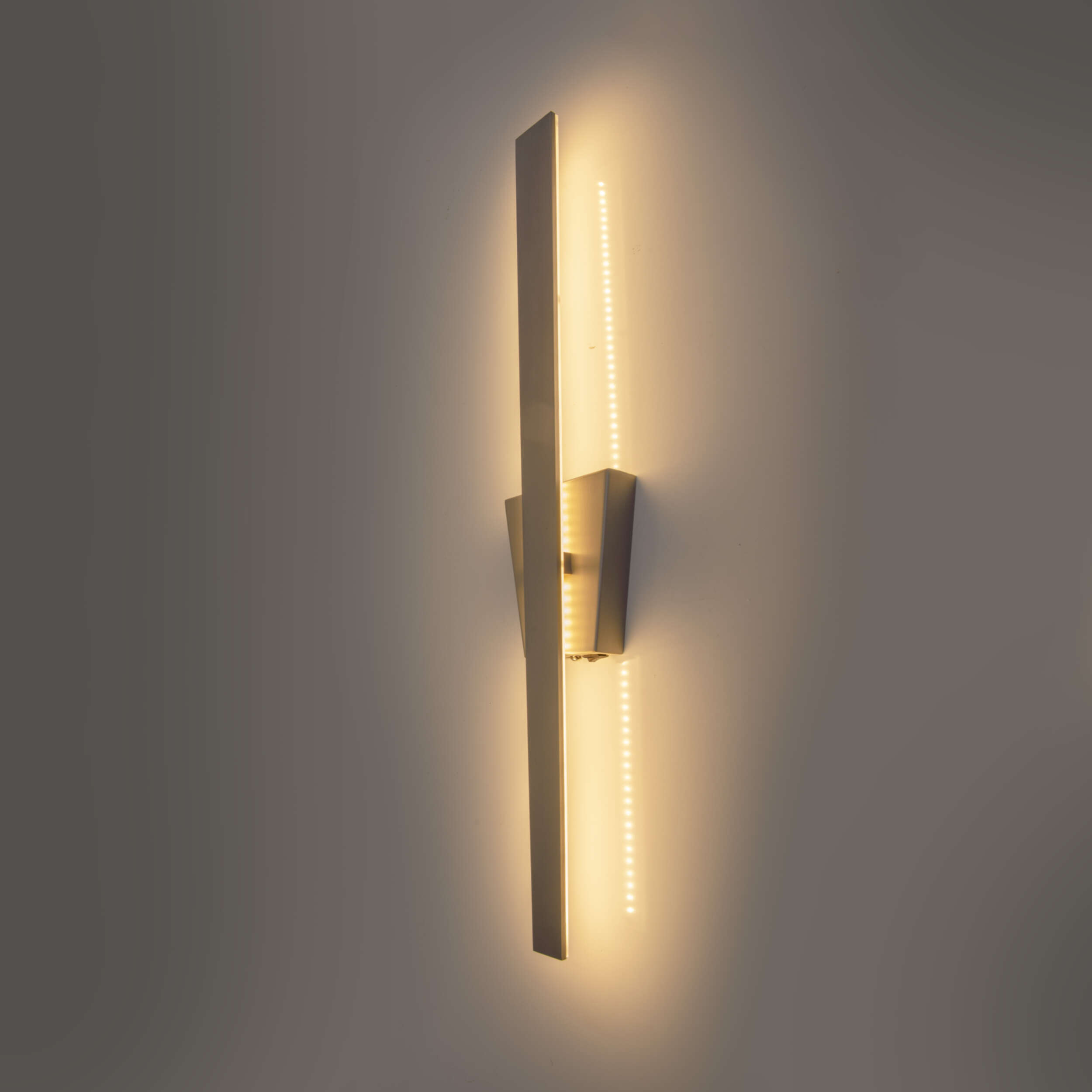Moderne Wandleuchte mit langem vertikalem Licht und abgewinkeltem Metalldesign an einer grauen Wand.