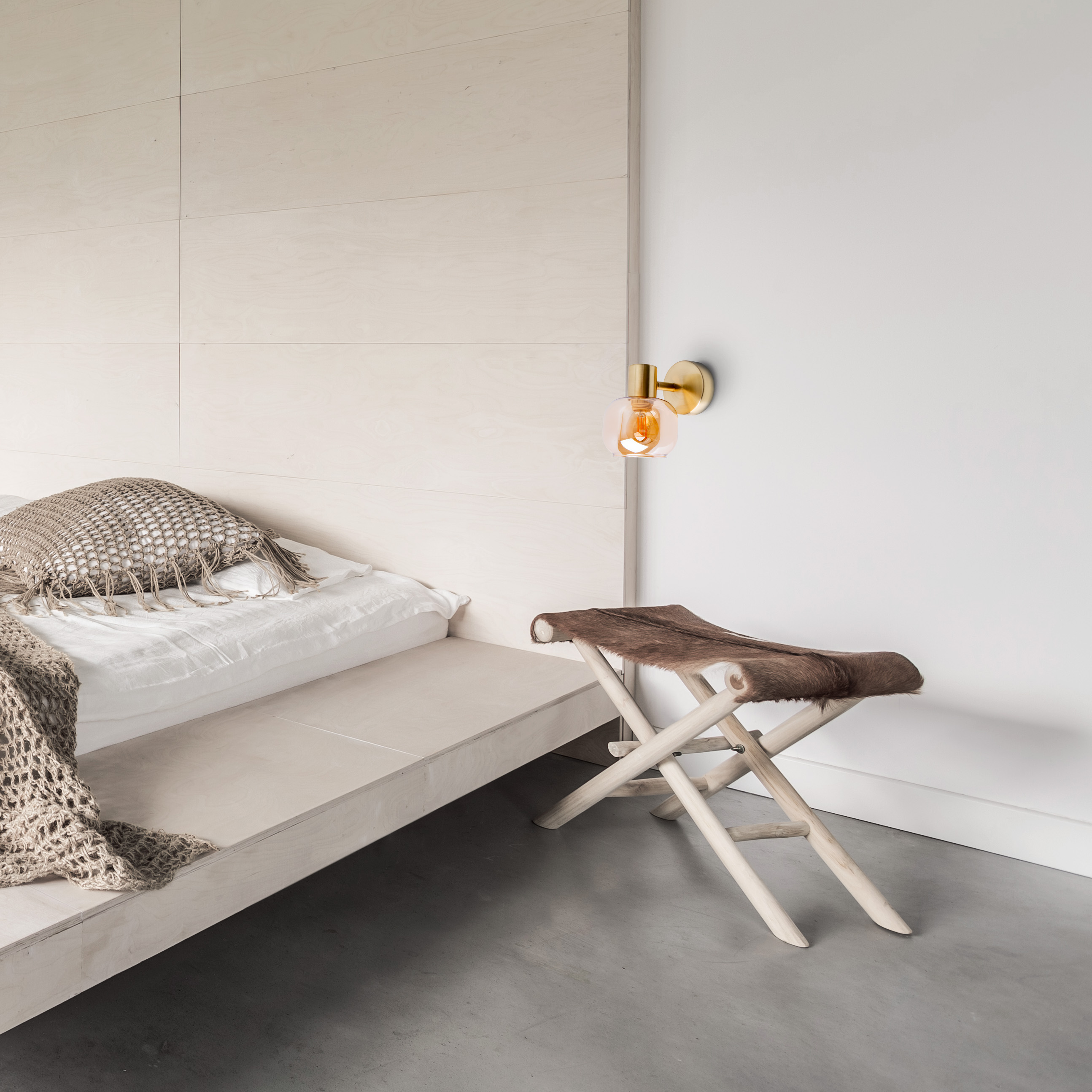 Schlafzimmer mit Wandlampe, Bett und Hocker mit Fellauflage.