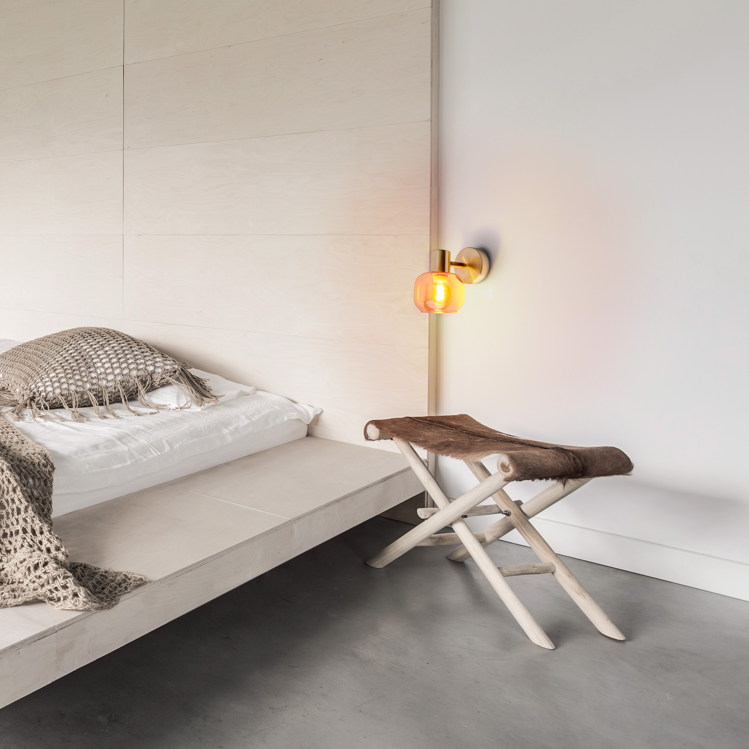 Schlafzimmer mit Bett, Hocker und Wandlampe. Neutrale Töne und Texturen.