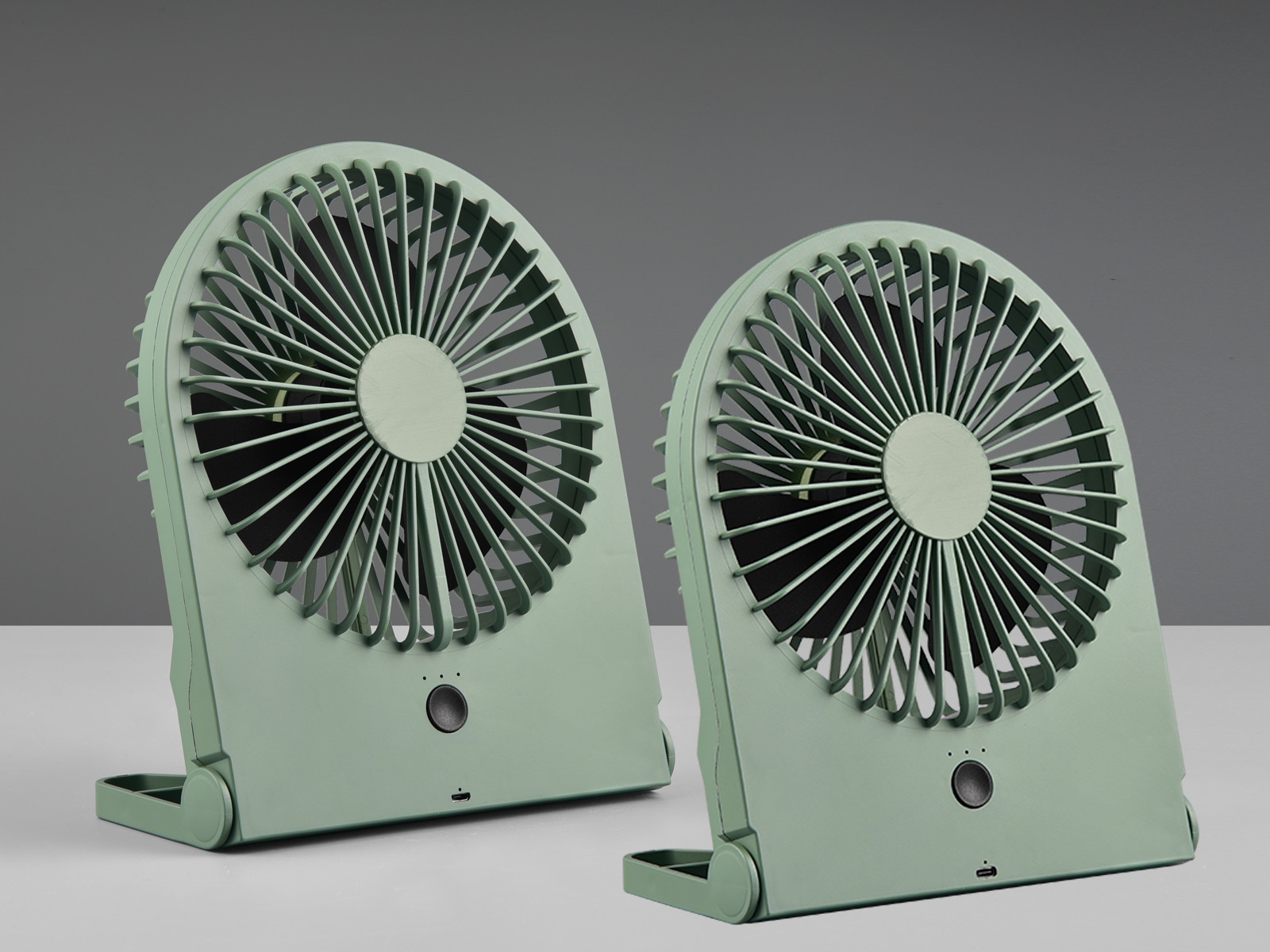 Zwei grüne, tragbare Ventilatoren mit gewölbten Schutzgittern auf heller Oberfläche, vor grauem Hintergrund.