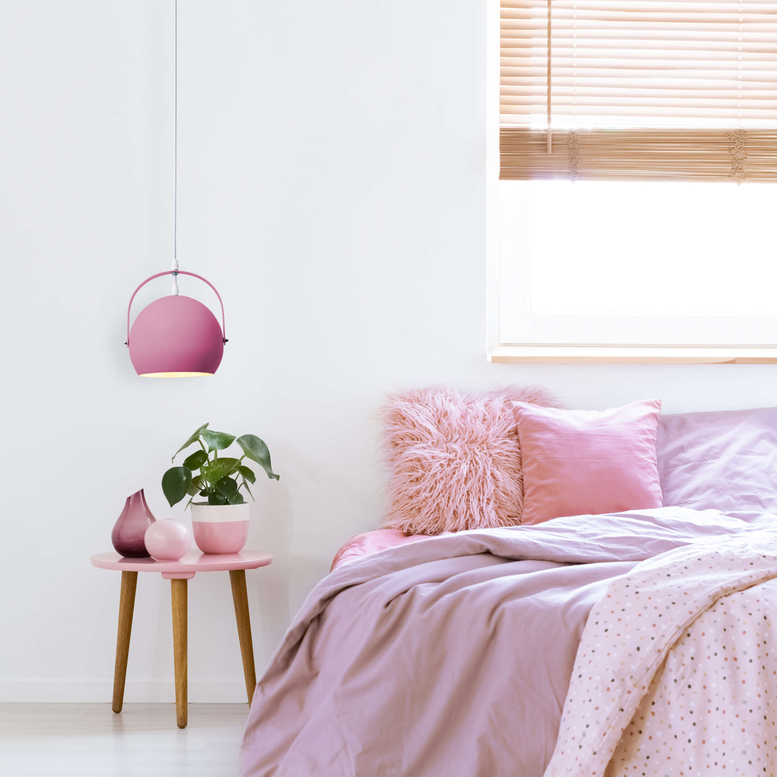 Rosa Schlafzimmer mit Pendelleuchte, rosa Bett und Beistelltisch.
