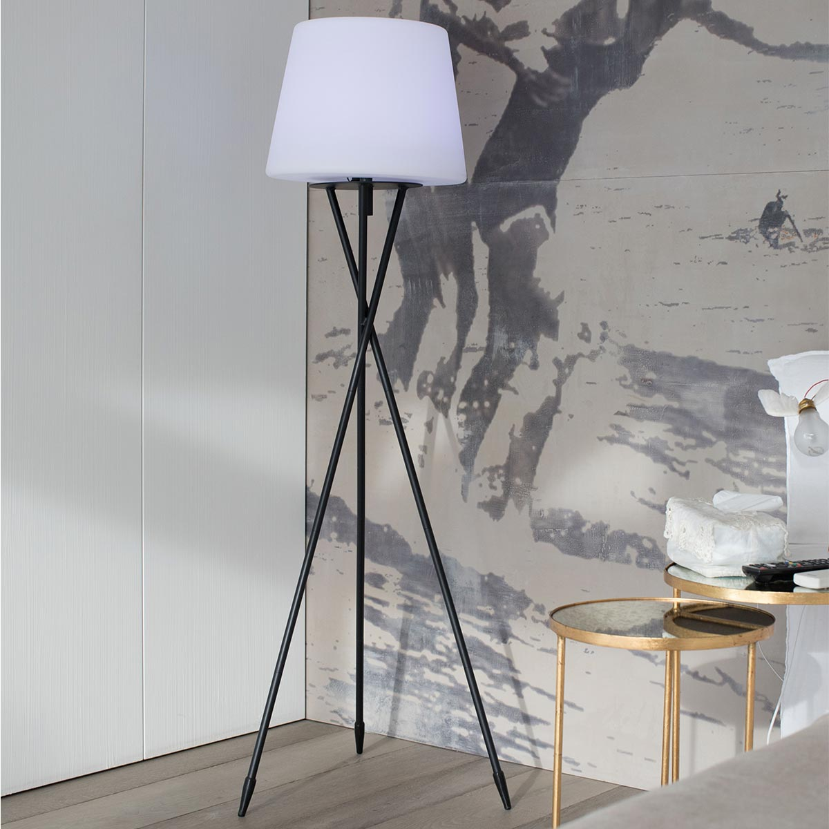Eine schwarze Stehlampe mit weißem Lampenschirm steht vor einer Wand mit einem Gemälde.