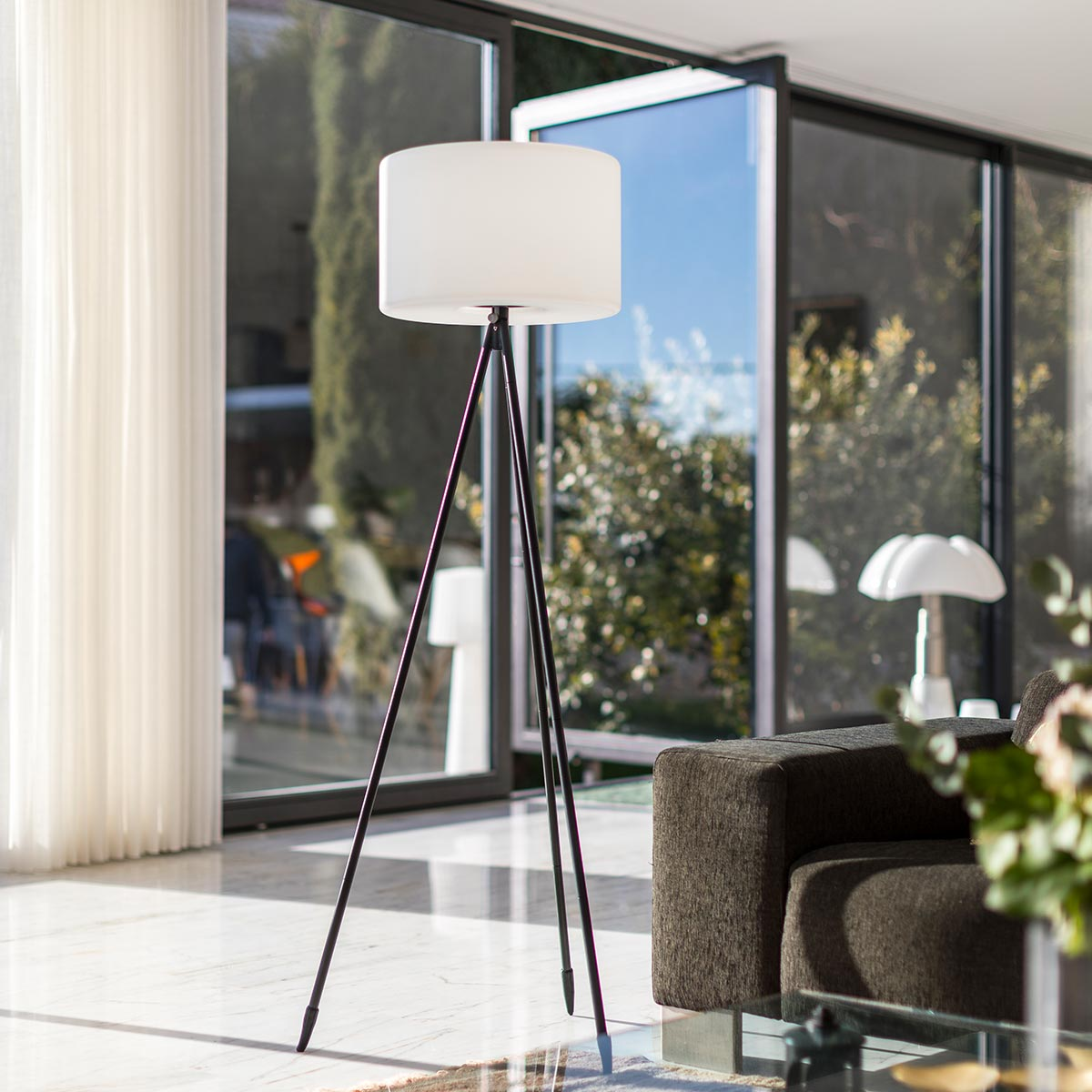 Una lampada da terra con paralume bianco, su un treppiede, in un salotto moderno.