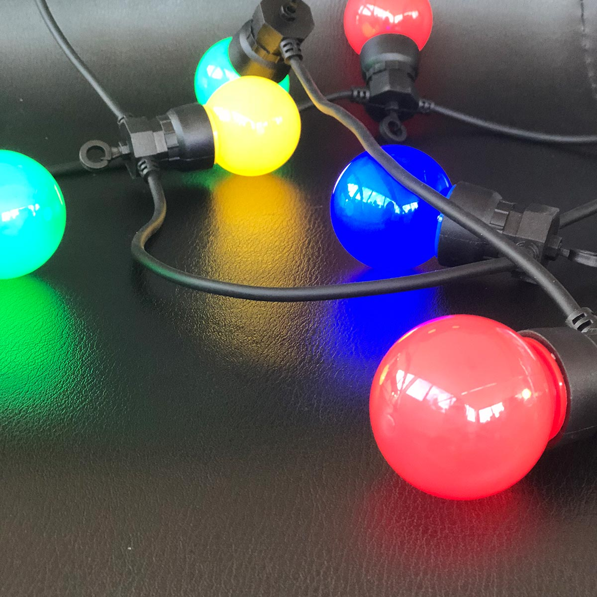 Eine Lichterkette mit bunten Lichtern, rot, blau, grün und gelb. Die Lichter befinden sich auf einer schwarzen Oberfläche.