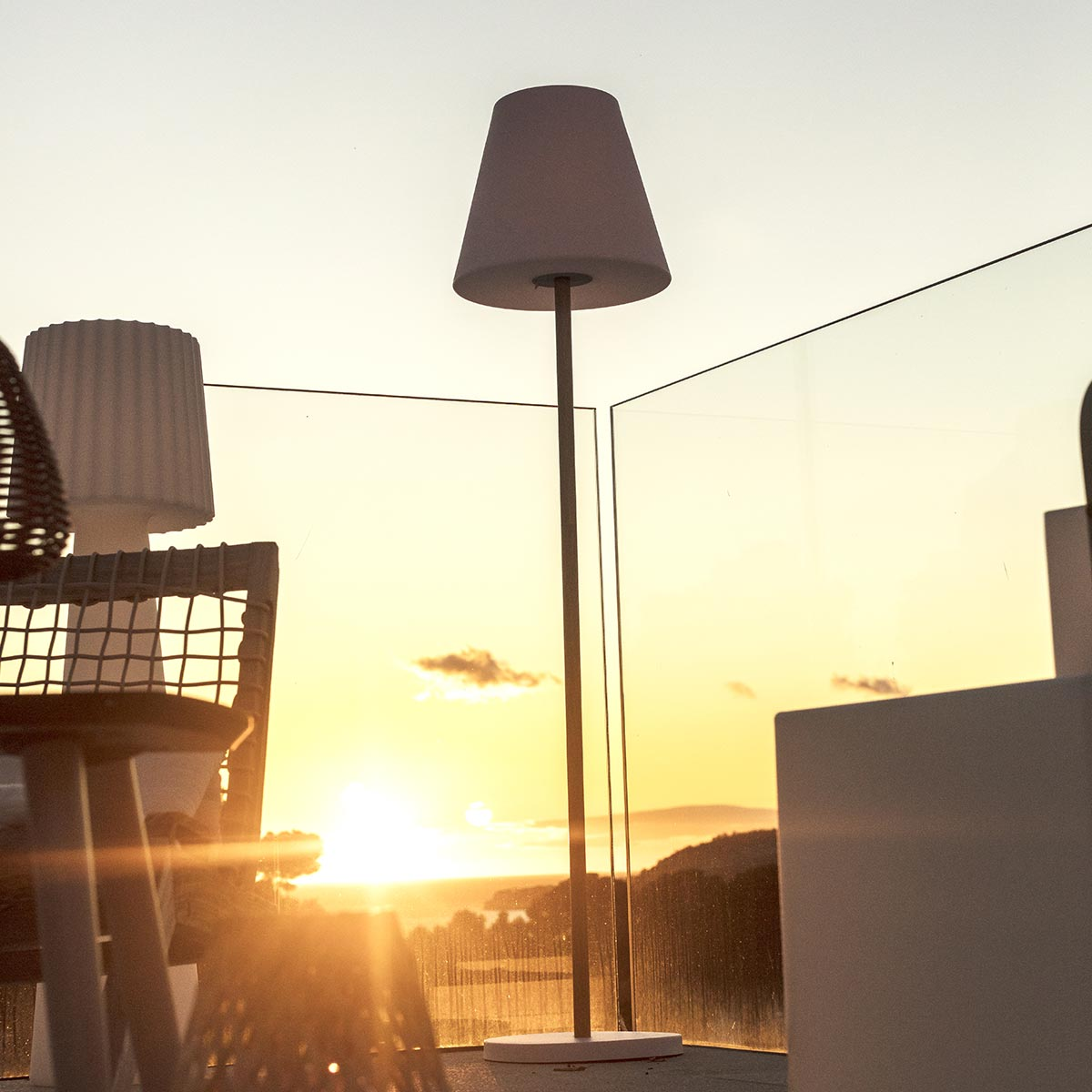 Außenlampe mit Lampenschirm, auf einer Terrasse mit Sonnenuntergang im Hintergrund.