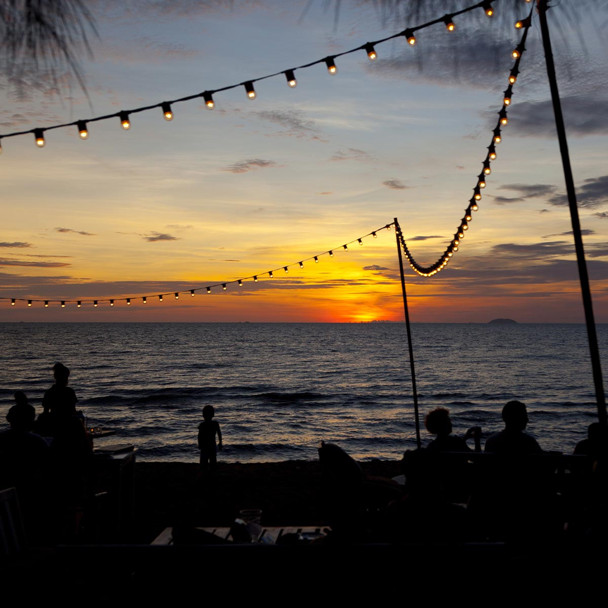 Sonnenuntergang über dem Meer. Menschen am Strand als Silhouette. Lichterkette. Dramatische Farben.