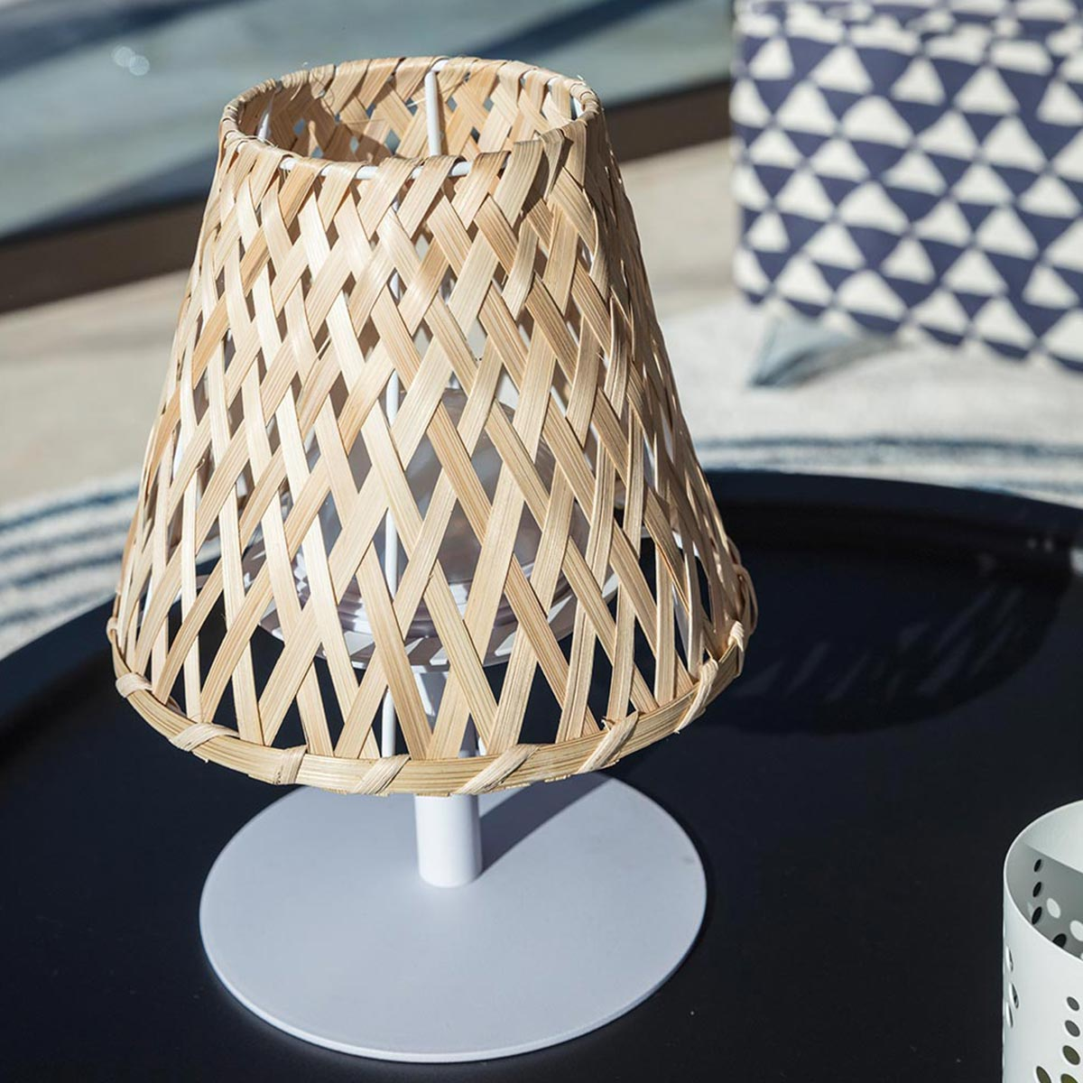 Eine kleine Tischlampe mit gewebtem, hellfarbigem Schirm auf weißem Sockel.