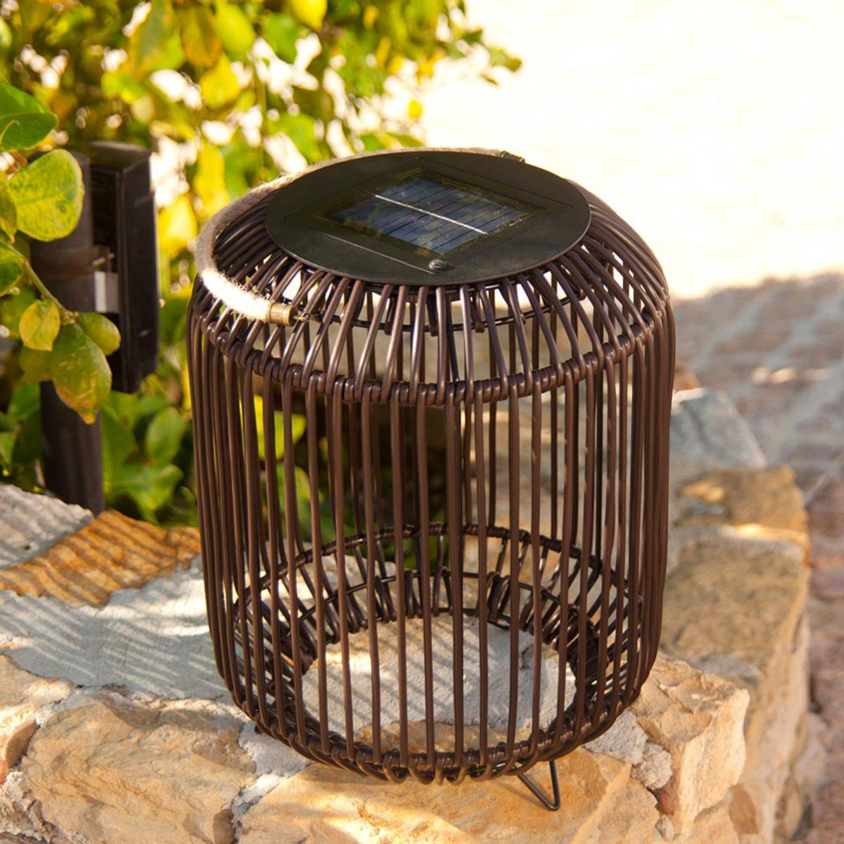 Braune Solar-Metalllaterne auf einer Steinoberfläche. Der Hintergrund ist ein Garten.