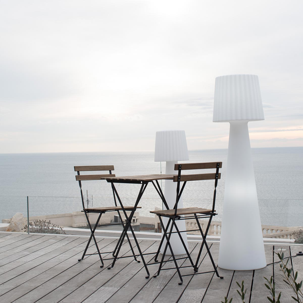 Outdoor-Sitzbereich mit Tisch, Stühlen und hohen weißen Lampen mit Meerblick.