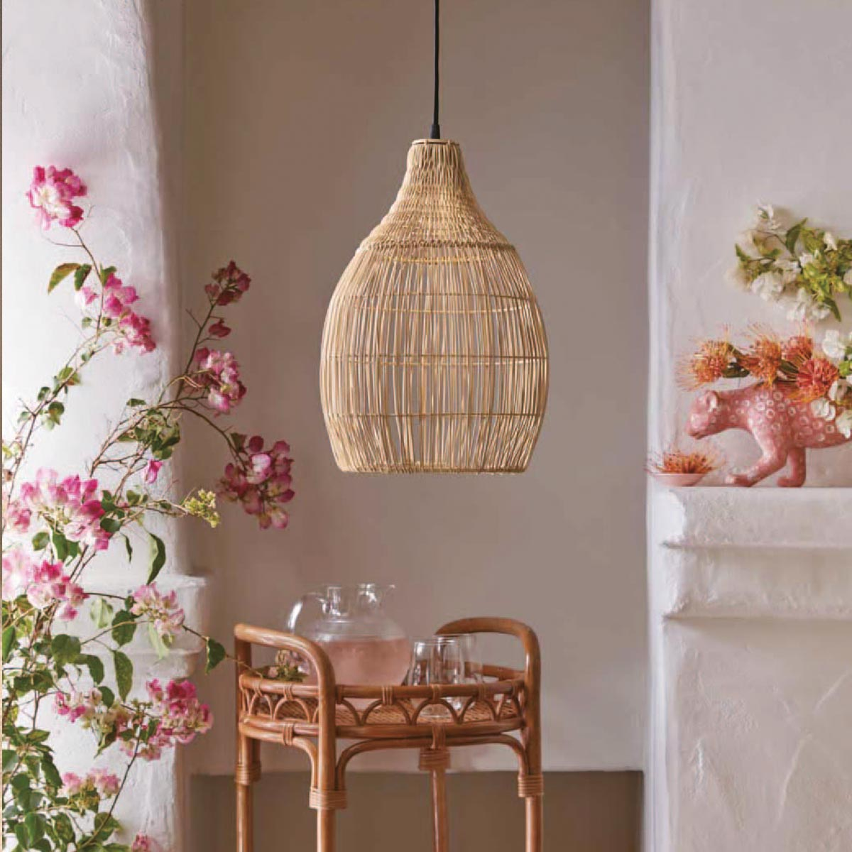 Eine gewebte Pendelleuchte aus Rattan hängt über einem Rattantisch, mit Blumen und Dekoration.