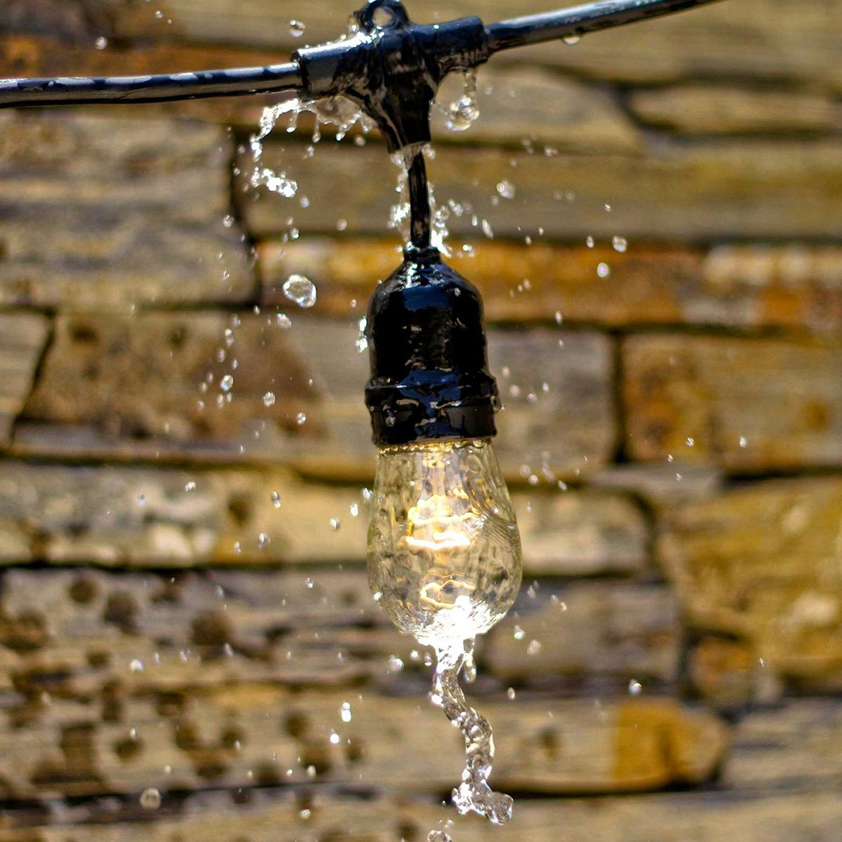 Eine beleuchtete Glühbirne mit Wassertropfen, die an einem schwarzen Draht hängen.