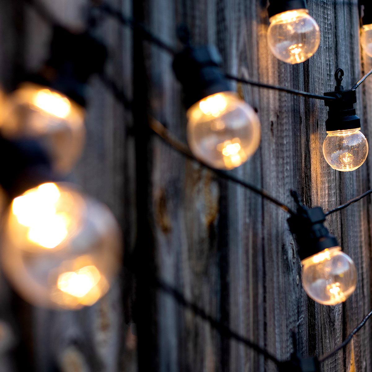 Lichterkette mit klaren Glühbirnen. Holz-Zaun-Hintergrund. Die Glühbirnen sind beleuchtet.