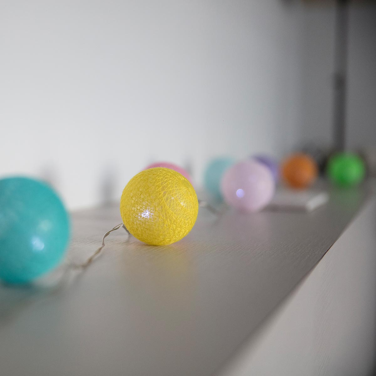Lichterkette, gelbes Licht im Fokus. Andere Lichter in verschiedenen Farben, auf einem weißen Regal.