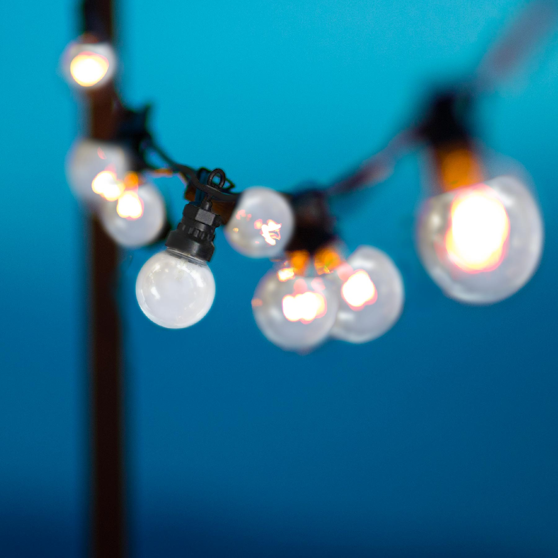 Lichterkette mit klaren Glühbirnen, vor verschwommenem blauem Hintergrund, erzeugt warmes Leuchten.