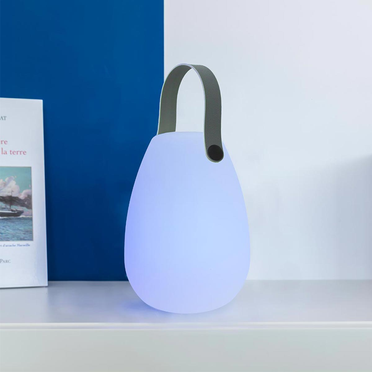 Eine weiße, eiförmige Lampe mit grauem Griff, die blau leuchtet.