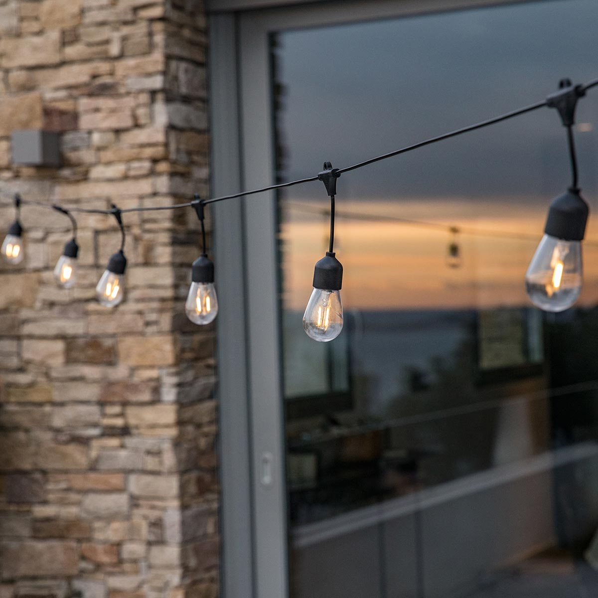 A string of outdoor lights with Edison bulbs against a brick wall at sunset.