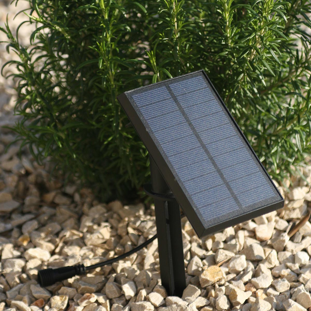A small black solar panel on a stand, in a bed of small stones.