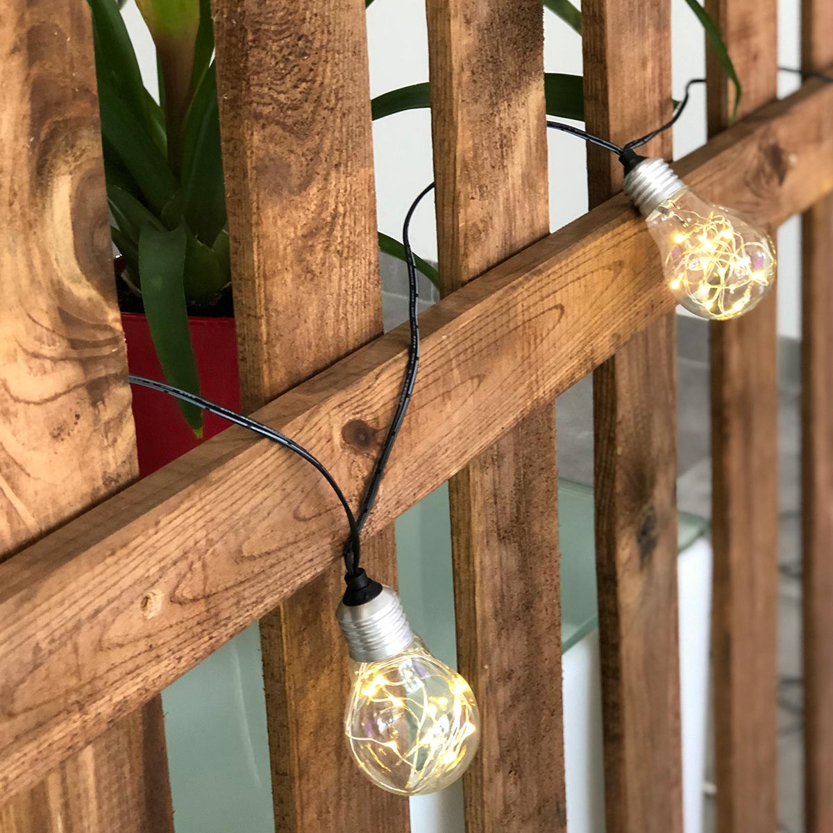 Holzzaun mit zwei beleuchteten Lichterketten. Lichter in Glühbirnen mit winzigen Lichtern.