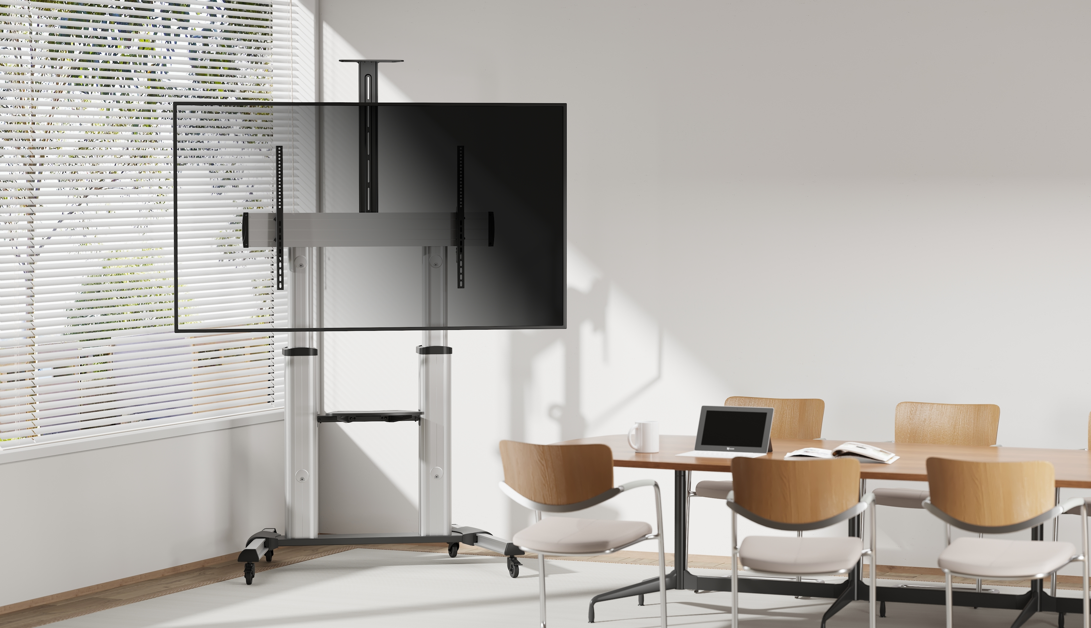 Sala de conferencias con TV grande en soporte rodante, mesa con portátil y sillas cerca de la ventana.