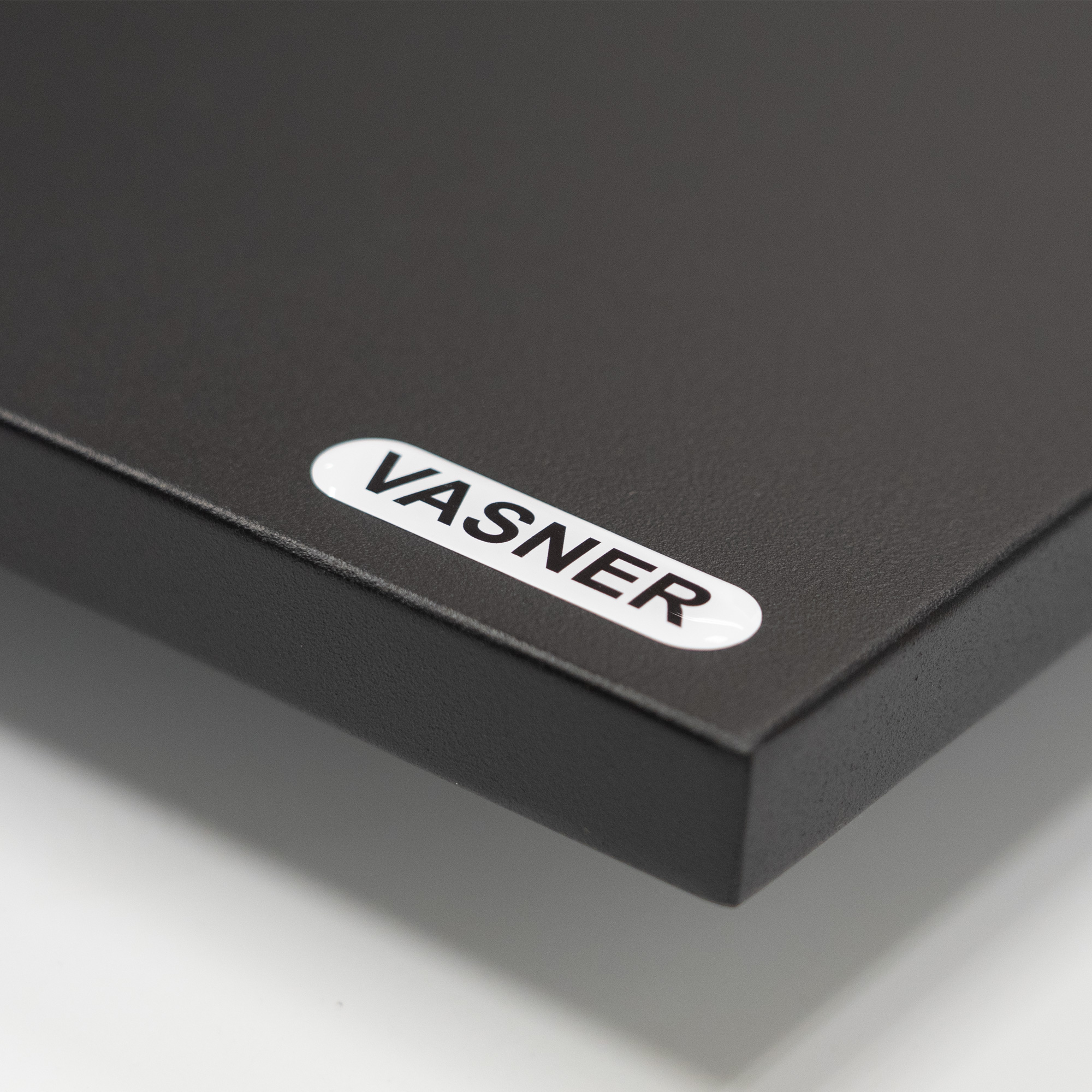 Ecke einer schwarzen Metalloberfläche mit weißem Aufkleber 'VASNER'.