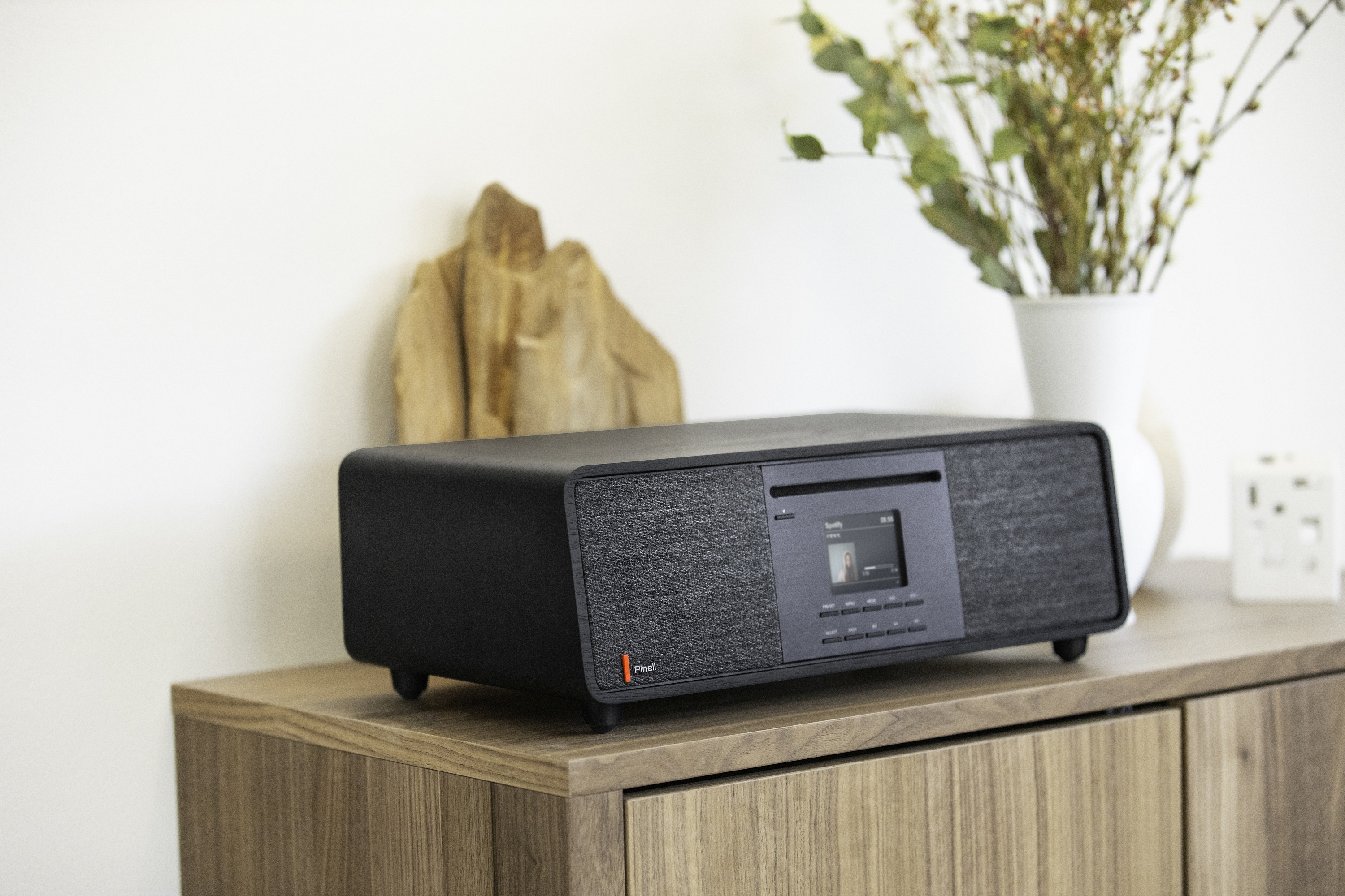 Black stereo system on wood cabinet, decorative vase and decor.