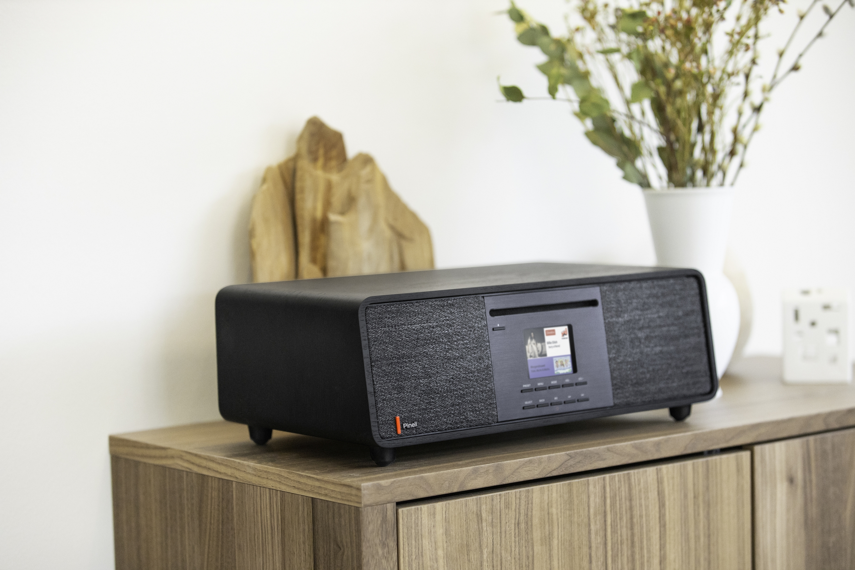 Black audio system on a wooden cabinet. White wall with decorations in the background.