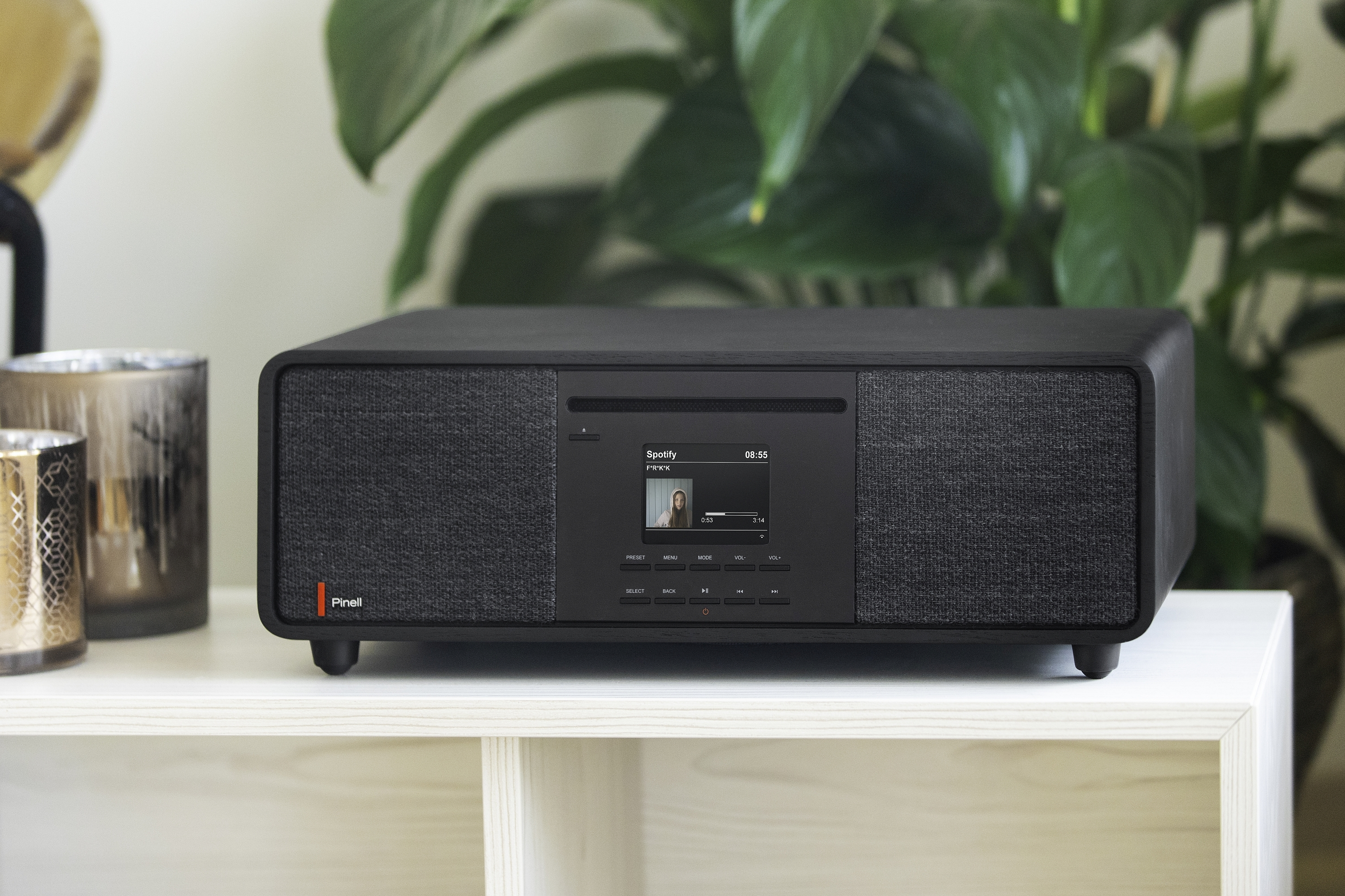 A black audio system on a white table with a plant in the background.
