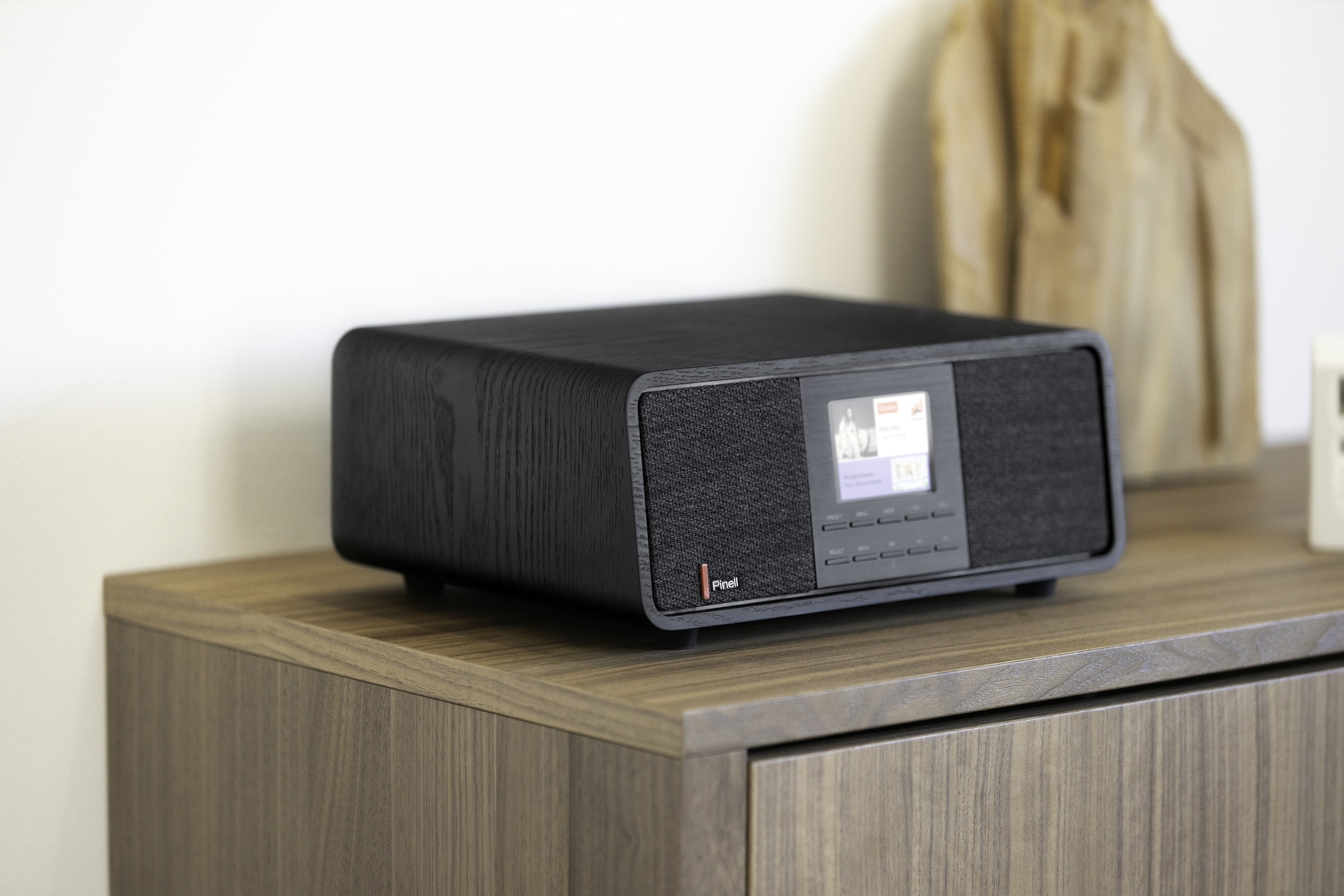 A black wooden digital music system with a screen, sitting on a wooden cabinet.