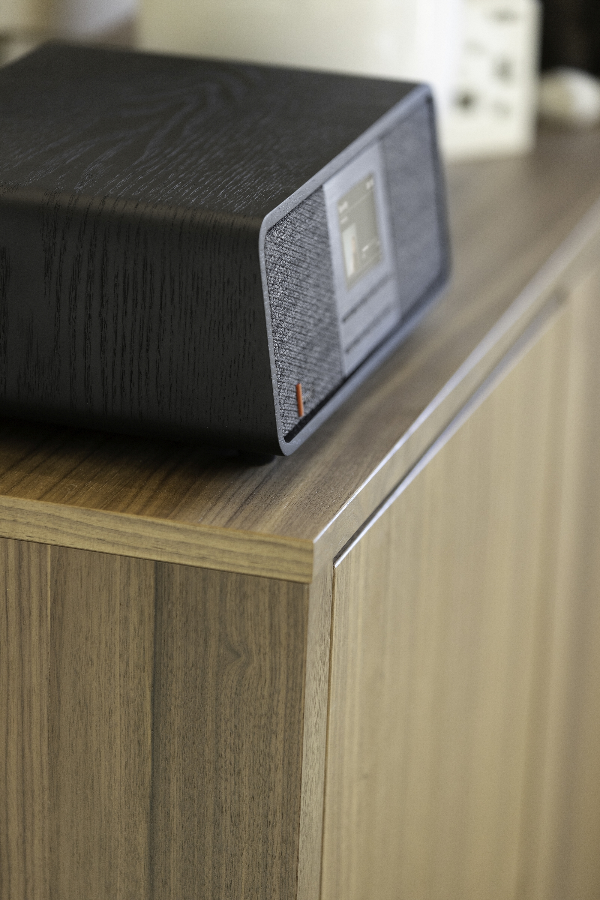 A black wooden speaker placed on a wooden cabinet. The speaker has a screen and buttons.