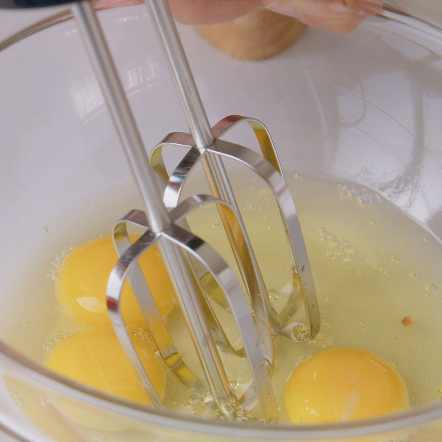 Huevos y un batidor en un cuenco transparente. Las yemas son amarillas y las claras transparentes y mezcladas.