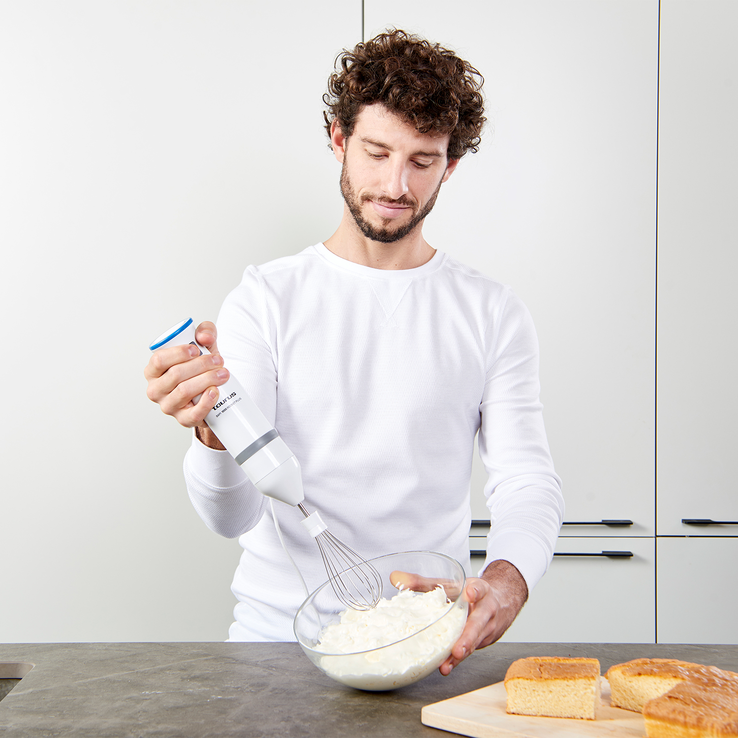 Hombre mezclando crema batida en un bol de vidrio con una batidora eléctrica.